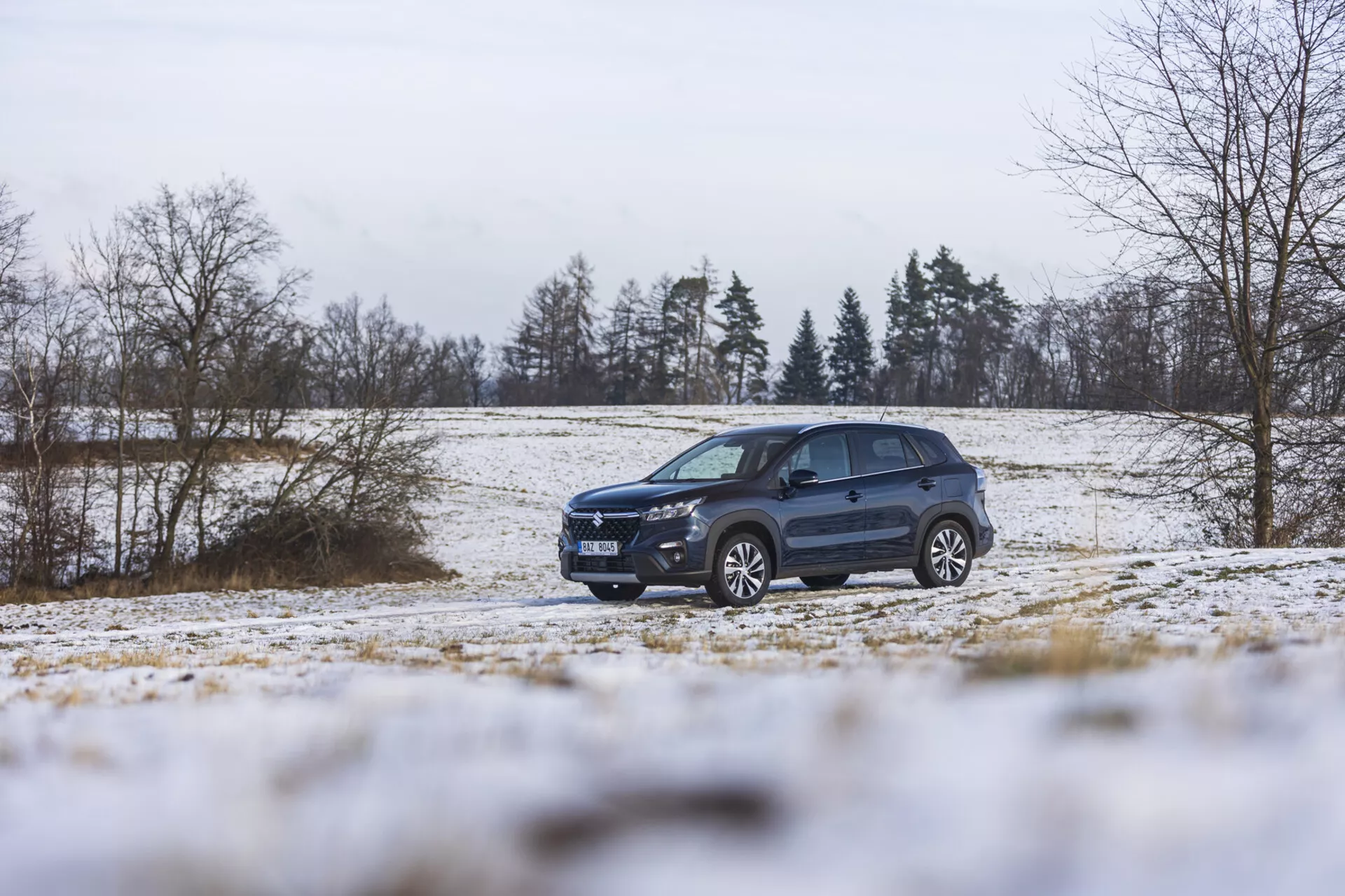 Suzuki S-Cross del 2022 in un paesaggio invernale con neve, che mostra il suo design dinamico, illuminazione avanzata, ruote in lega, e barre sul tetto, enfatizzando il suo stile da SUV e la capacità fuoristrada.