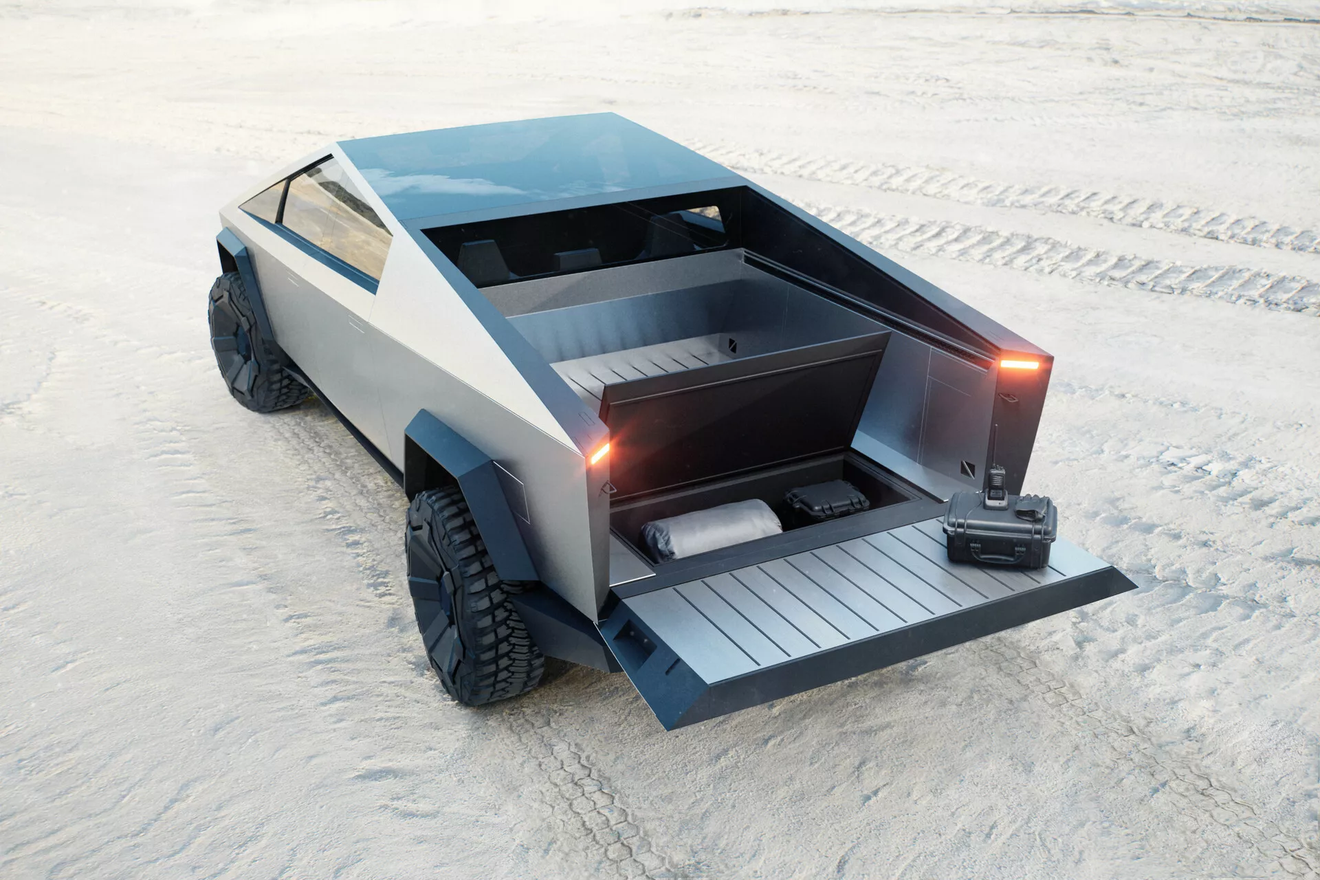 Futuristico Tesla Cybertruck 2021 (1ª generazione) parcheggiato su una superficie sabbiosa, catturato da una vista elevata posteriore di tre quarti. Il design angolare e poligonale presenta un pianale con portellone motorizzato abbassato, rivelando una rampa integrata. Il veicolo include anche una copertura tonneau bloccabile, grandi pneumatici fuoristrada e una finitura grigia opaca che contribuisce alla sua estetica minimalista e industriale. Non ci sono maniglie delle portiere tradizionali né specchietti laterali visibili, suggerendo maniglie retrattili e specchietti basati su telecamera. Si ipotizza che sia elettrico, concentrandosi sulla praticità e la capacità fuoristrada.