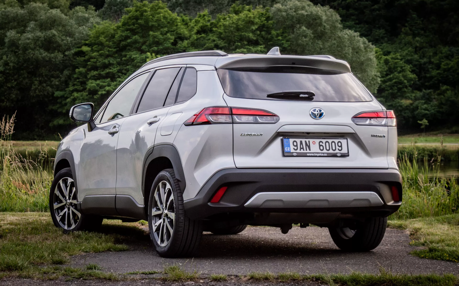 Vista posteriore tre quarti della Toyota Corolla Cross 2022 con fanali posteriori LED, badge ibrido e sensori di assistenza al parcheggio