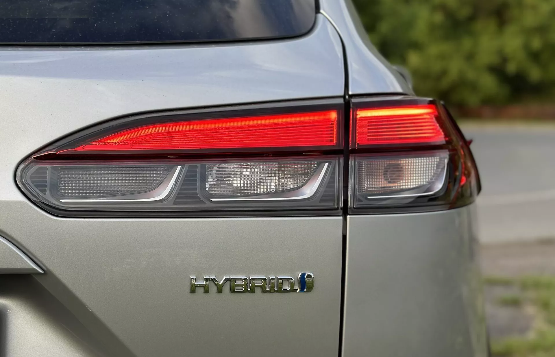 Primo piano dell'angolo posteriore sinistro della Toyota Corolla-Cross 2022 mostrando il design del fanale posteriore LED e l'emblema HYBRID con un focus sulla tecnologia ecocompatibile del veicolo e finitura lucida in un colore grigio chiaro smorzato