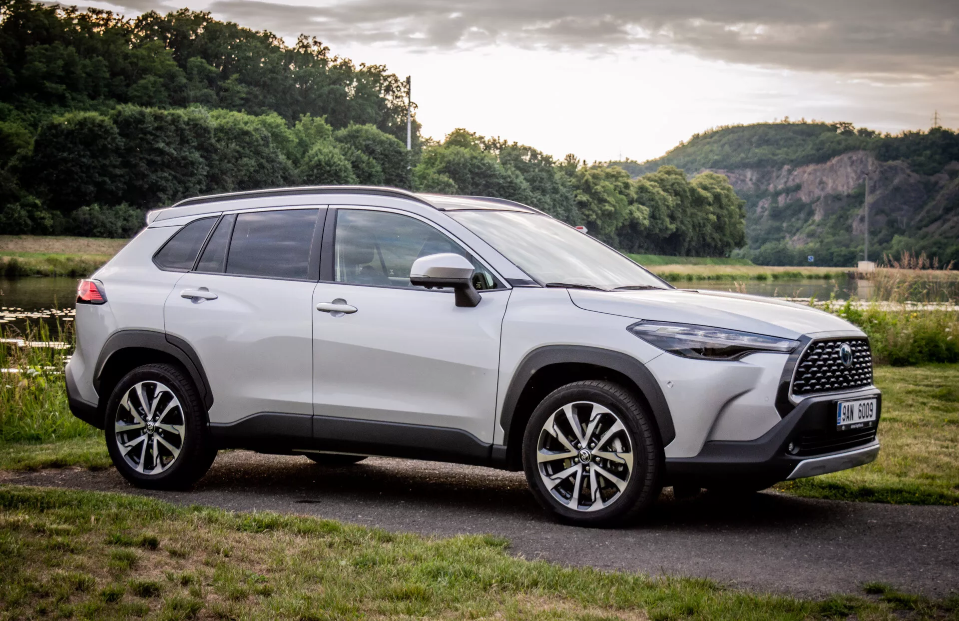 SUV Toyota Corolla Cross 2022 parcheggiata all'aperto, che mostra il suo design moderno da un angolo frontale di tre quarti con focus sulla griglia, ruote in lega e profilo laterale contro un sfondo naturale