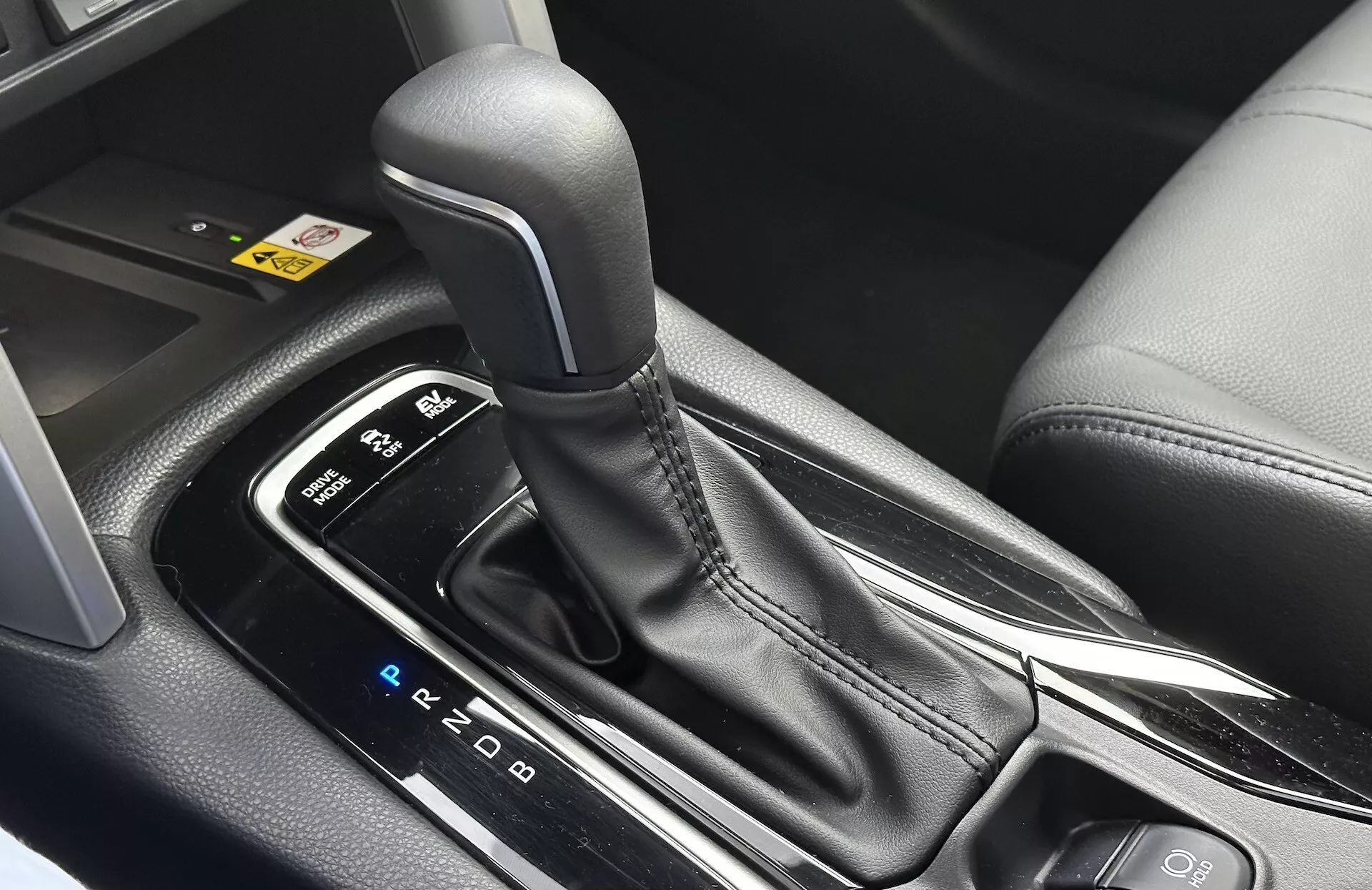 Vista interna dettagliata della Toyota Corolla Cross 2022 che mostra la leva del cambio automatico con disposizione PRND visibile, circondata da una consolle centrale elegante con rifiniture in plastica nera e accenti metallici, evidenziando il design ergonomico e le caratteristiche tecnologiche moderne