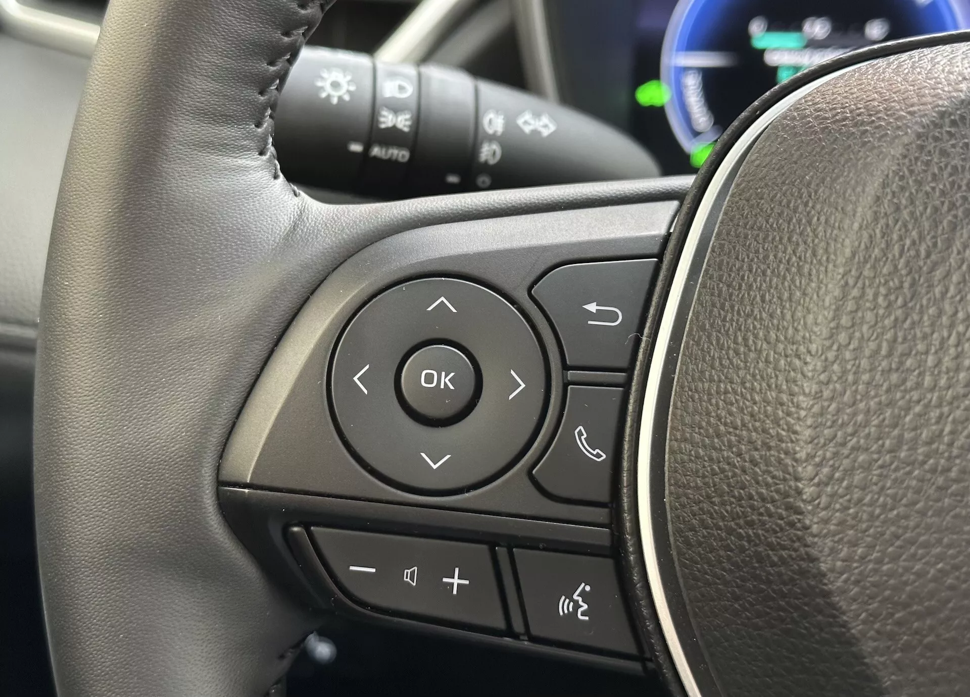 Vista dettagliata del volante di Toyota Corolla Cross 2022 con focus sui controlli multifunzione sul raggio sinistro con texture simile alla pelle e pulsanti chiaramente contrassegnati per l'audio, la connettività telefonica Bluetooth, comandi vocali e navigazione attraverso il sistema di informazione del conducente