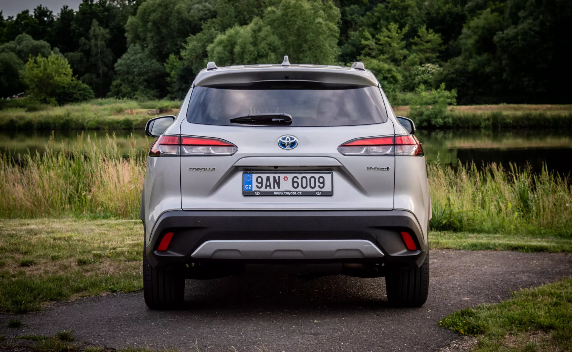 Vista posteriore di un modello ibrido Toyota C-HR che mostra luci posteriori a LED, paraurti integrato con diffusore e riflettori, antenna montata sul tetto e ruote in lega, impostato su uno sfondo naturale