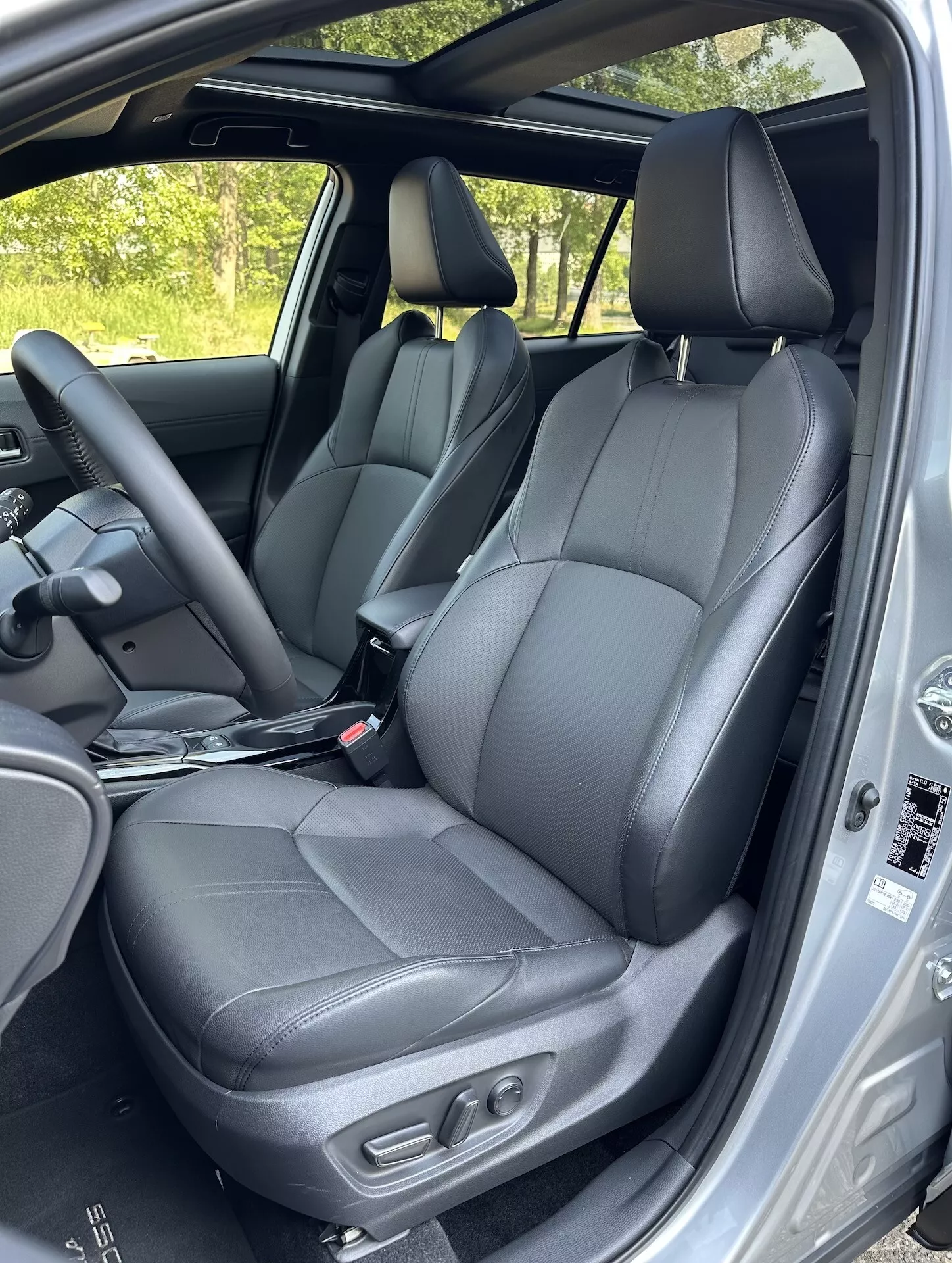 Vista interna della Toyota Corolla Cross 2022 che evidenzia i sedili anteriori in pelle nera con comandi di regolazione, parte dei sedili posteriori, il volante e le caratteristiche di sicurezza del telaio della porta alla luce naturale del giorno