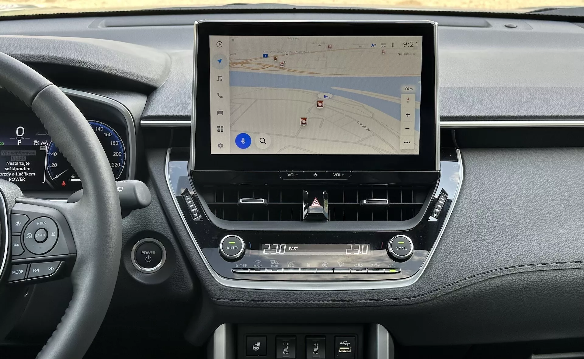 Interni della Toyota Corolla Cross 2022 che mostrano una console centrale moderna con un grande display touchscreen verticale per la navigazione, circondato da eleganti elementi del cruscotto che incorporano dettagli in pelle, cluster di strumentazione digitale accanto al volante e controlli tattili ergonomici per clima e audio, impostati in luce naturale.