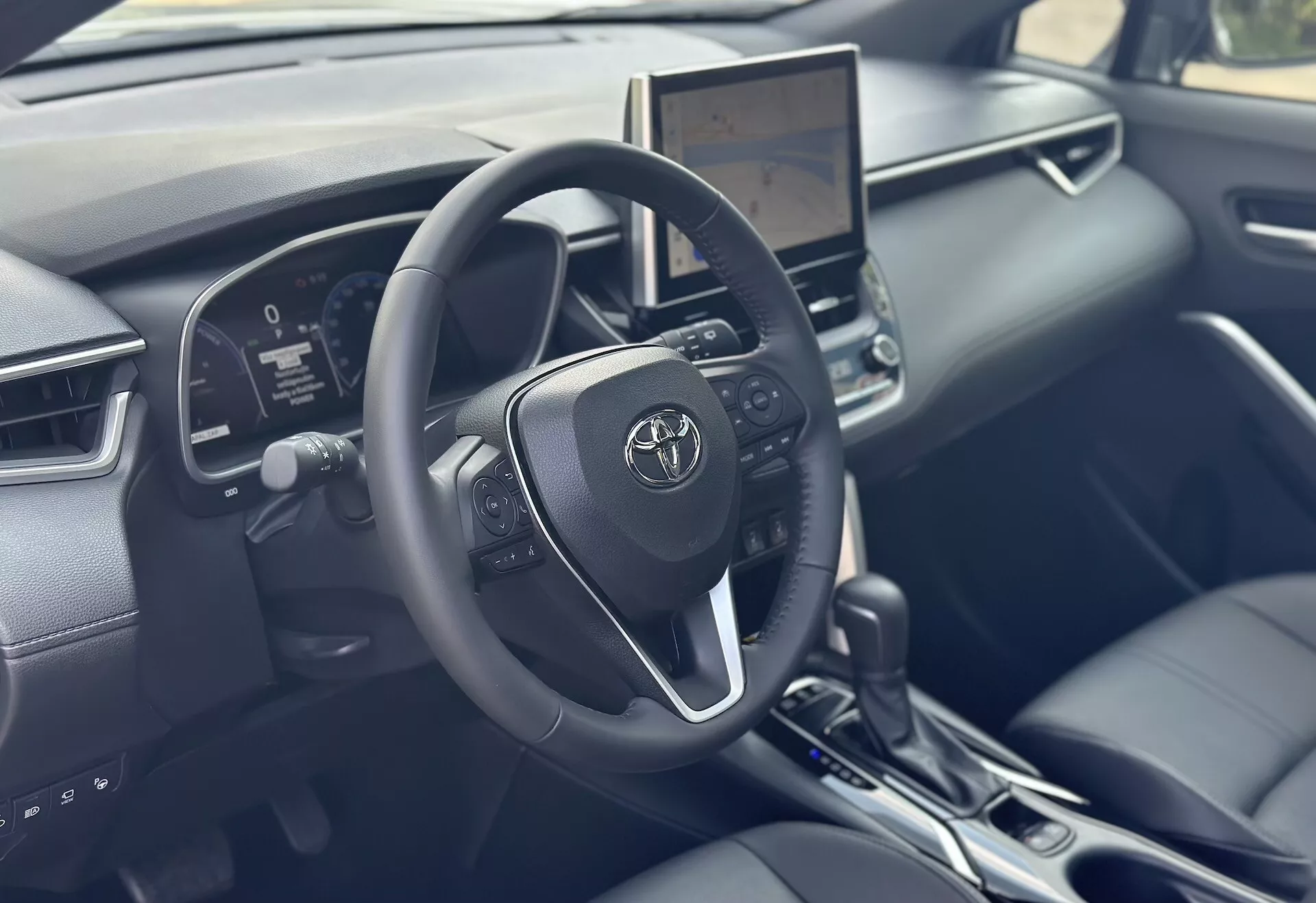 Interni del Toyota Corolla Cross 2022 focalizzati sul lato guidatore con volante dettagliato, cruscotto digitale e touchscreen infotainment centrale dotati di tecnologia moderna e accenti in pelle nera