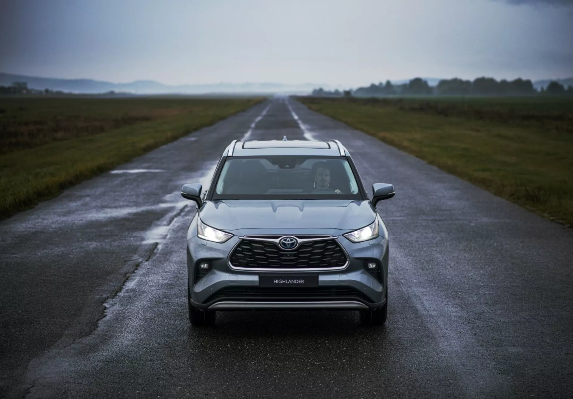 Toyota Highlander 2021 posizionata su una strada bagnata evidenziando il suo design frontale, tempo nuvoloso, con fari LED, luci antinebbia, una grande griglia e tecnologia di sicurezza avanzata