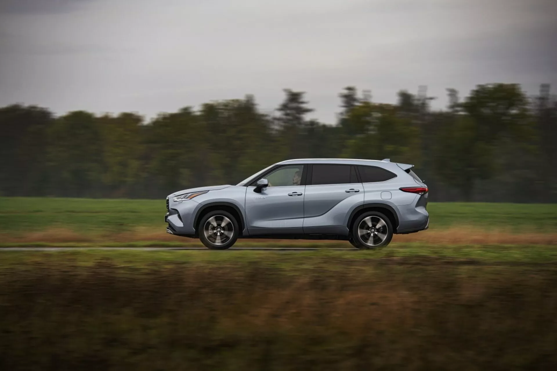 Toyota Highlander 2021 in movimento, moderno SUV argento catturato da un profilo laterale, mostrando design aerodinamico e caratteristiche tecnologiche