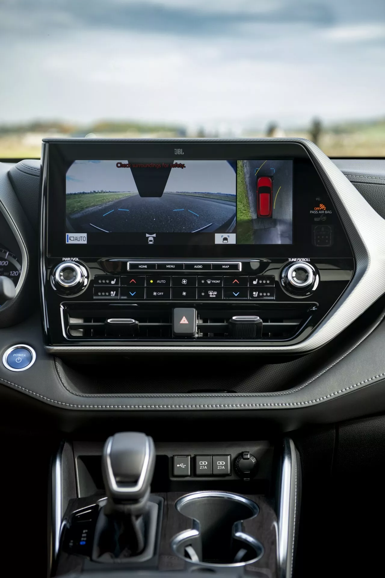 Interno della Toyota Highlander 2021 con enfasi sulla console centrale dotata di touchscreen orizzontale che mostra la telecamera posteriore e l'assistente al parcheggio, comandi per il clima a doppia zona e leva del cambio automatico