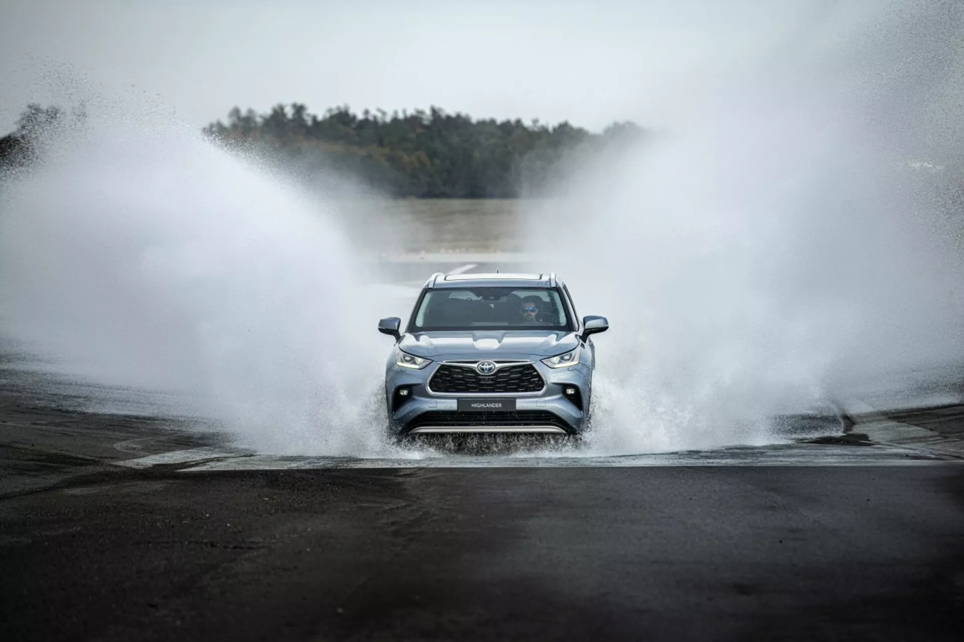 Toyota Highlander 2021 che guida frontalmente attraverso l'acqua, mostrando la griglia anteriore, i fari LED e un design sportivo in un contesto avventuroso