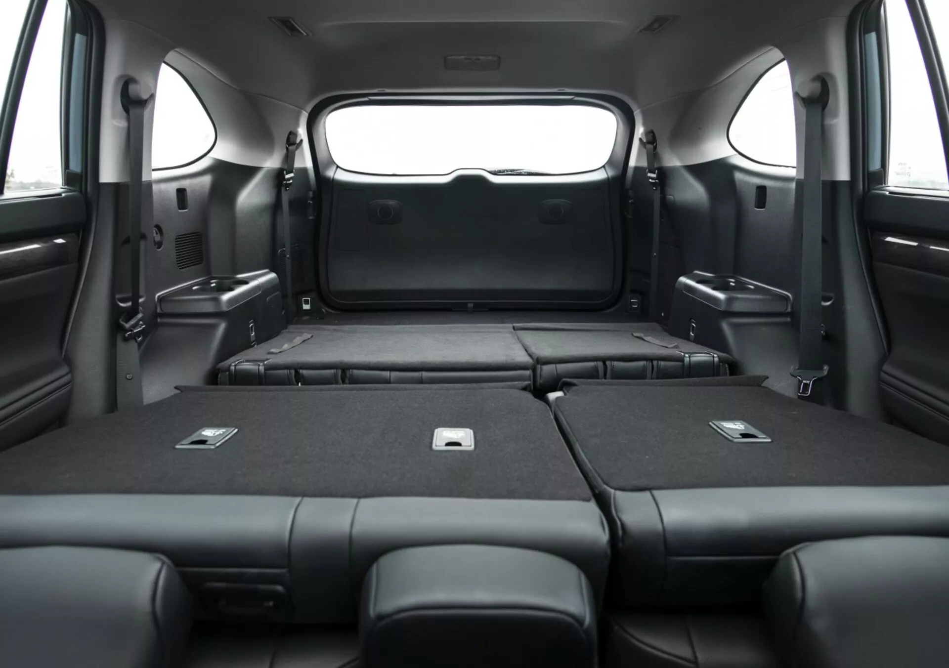 Vista interna della Toyota Highlander 2021, che mostra l'area di carico espansa con i sedili posteriori abbattuti, evidenziando l'ampia capacità di bagaglio e l'elegante tappezzeria nera da una prospettiva interna.