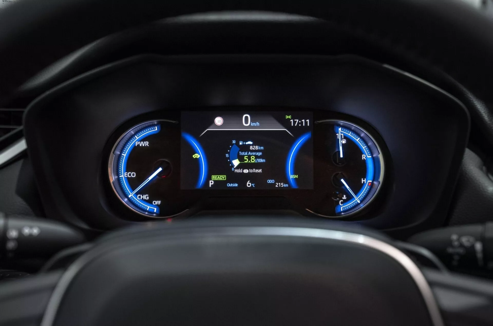 Primo piano del quadro strumenti della Toyota RAV4 2019 con indicatori ibridi di potenza, tachimetro e display digitale centrale che mostra posizione ferma, efficienza del carburante e temperatura esterna dal punto di vista del conducente.