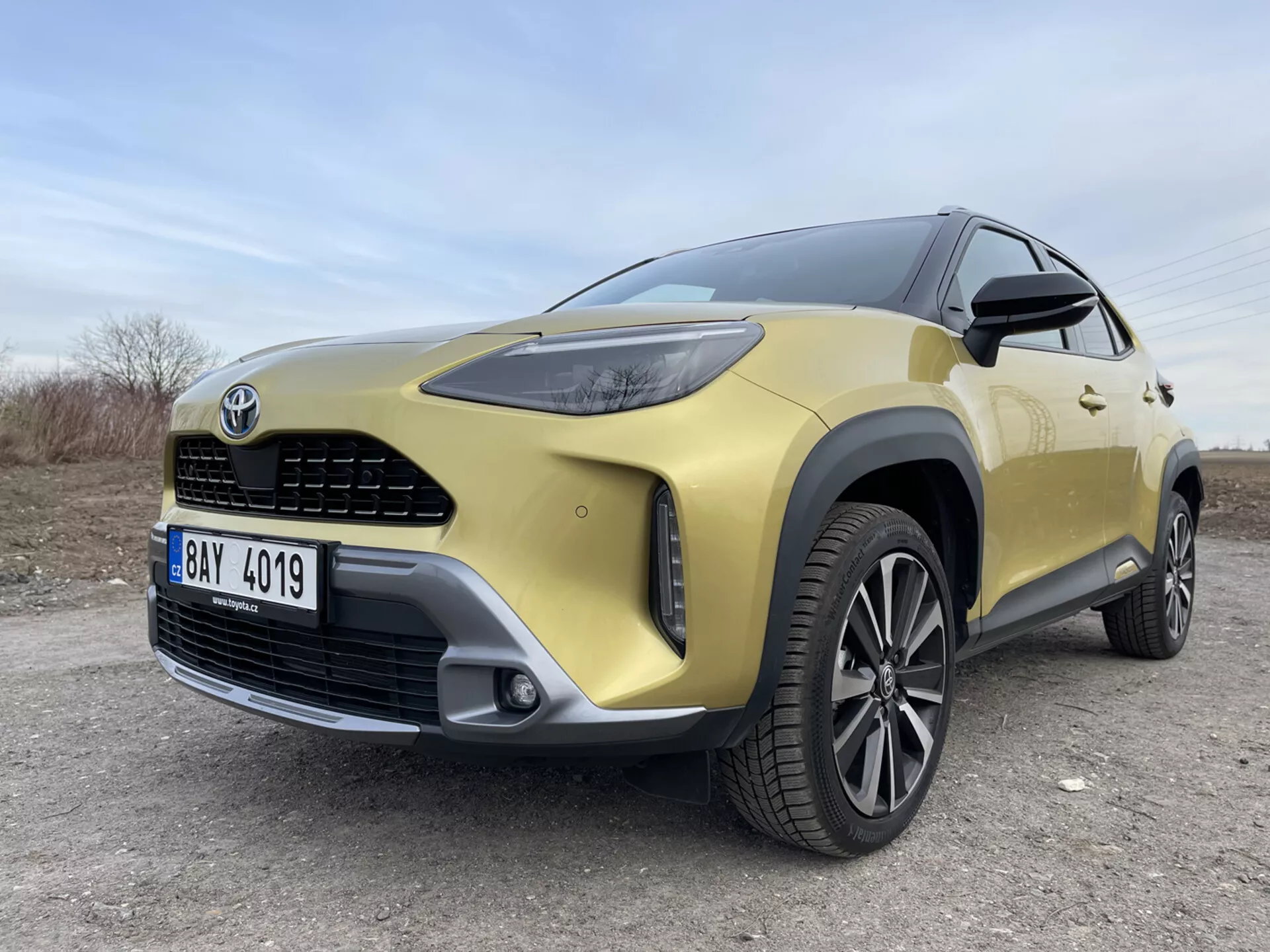 SUV Toyota Yaris-Cross 2021 in oro che mostra il suo quarto anteriore sinistro da una vista angolare bassa mettendo in evidenza i fari LED, la griglia frontale, il paraurti, il cerchio in lega e gli elementi di design moderno su una superficie non asfaltata