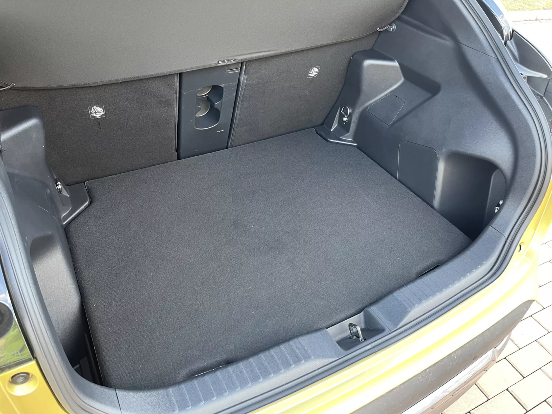 Vista interna del bagagliaio della Toyota Yaris Cross 2021 che mostra uno spazio di carico vuoto, rivestito in moquette, con lati in plastica stampata, aree rientranti per lo stoccaggio, tagli per l'accesso alle attrezzature e indentazioni dei sedili posteriori ribaltabili