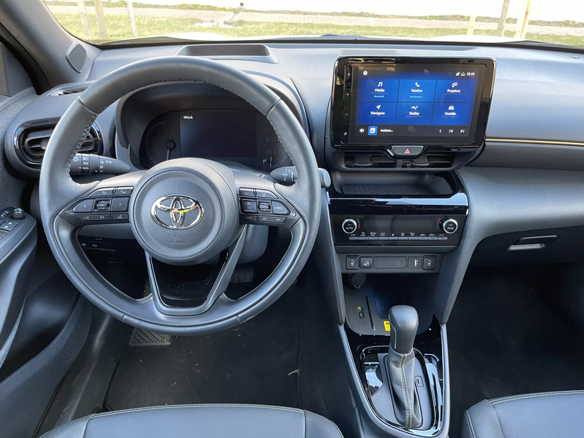 Vista interna della Toyota Yaris Cross 2021 dal lato del passeggero anteriore, mostrando cruscotto, volante con comandi integrati, sistema di infotainment touchscreen, leva del cambio automatico, e caratteristiche di sedute e design elegante in tema scuro