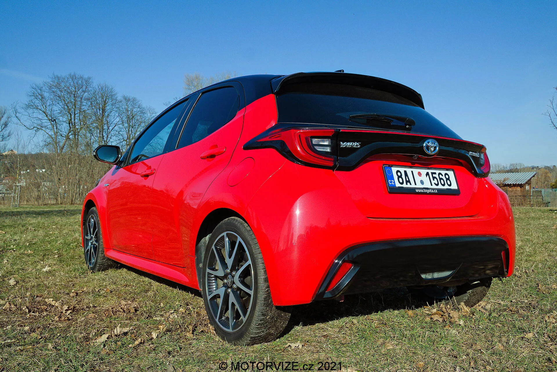 Vista tre quarti posteriore di una hatchback Toyota Yaris 2020 rosso brillante, vista da un'angolazione bassa, che mette in risalto le linee di design e le caratteristiche chiave come le luci posteriori a LED, lo spoiler posteriore, l'antenna a pinna di squalo e i cerchi in lega a più razze con finitura scura. La foto cattura il dettaglio del retro e parte del profilo laterale alla luce del giorno, esibendo la sua estetica sportiva ed elementi moderni.