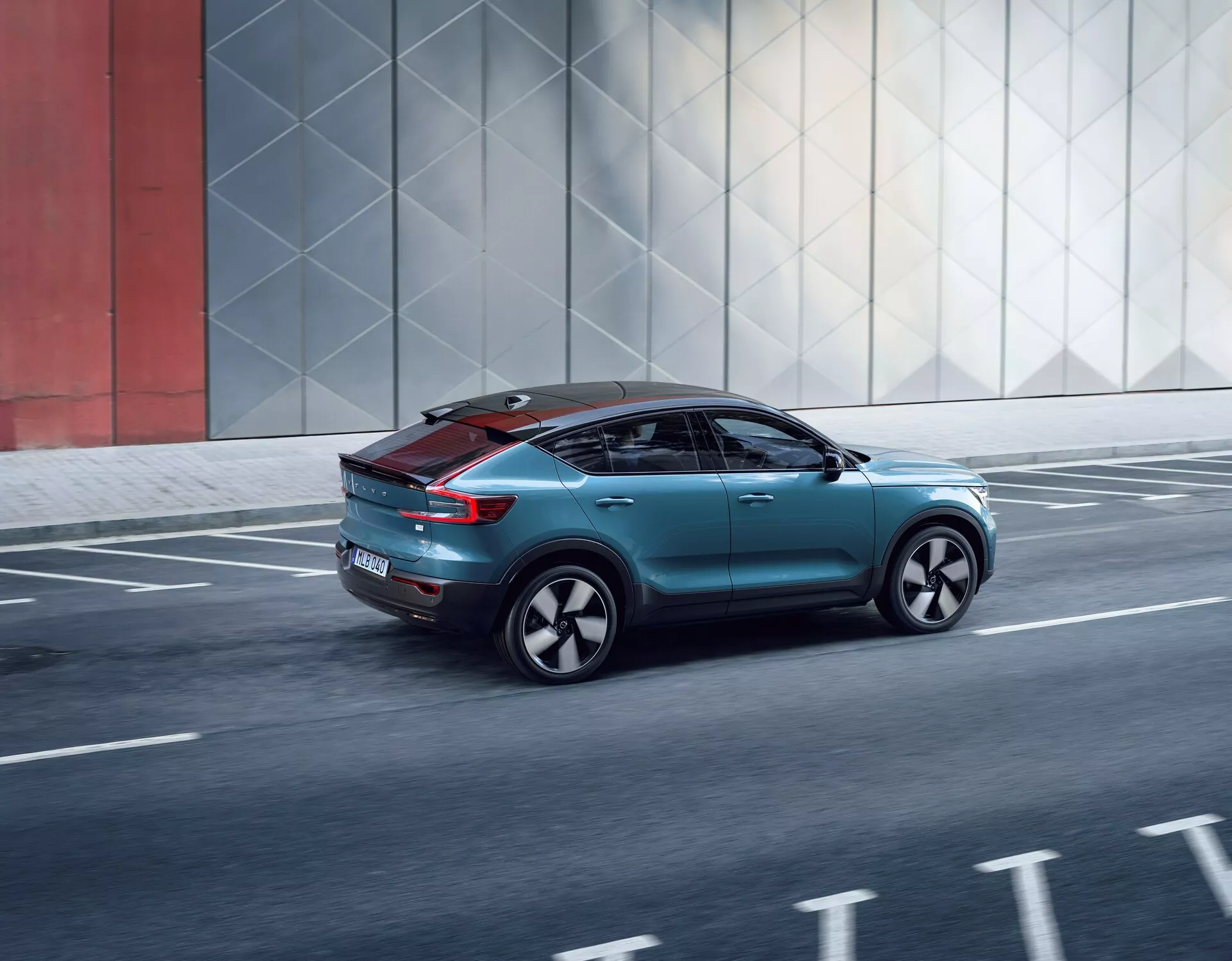 Vista dinamica a tre quarti posteriore della Volvo C40 2021, che mostra il suo design elegante, elementi aerodinamici, fanali posteriori moderni, ruote personalizzate e tetto panoramico, mentre si muove lungo una strada urbana.