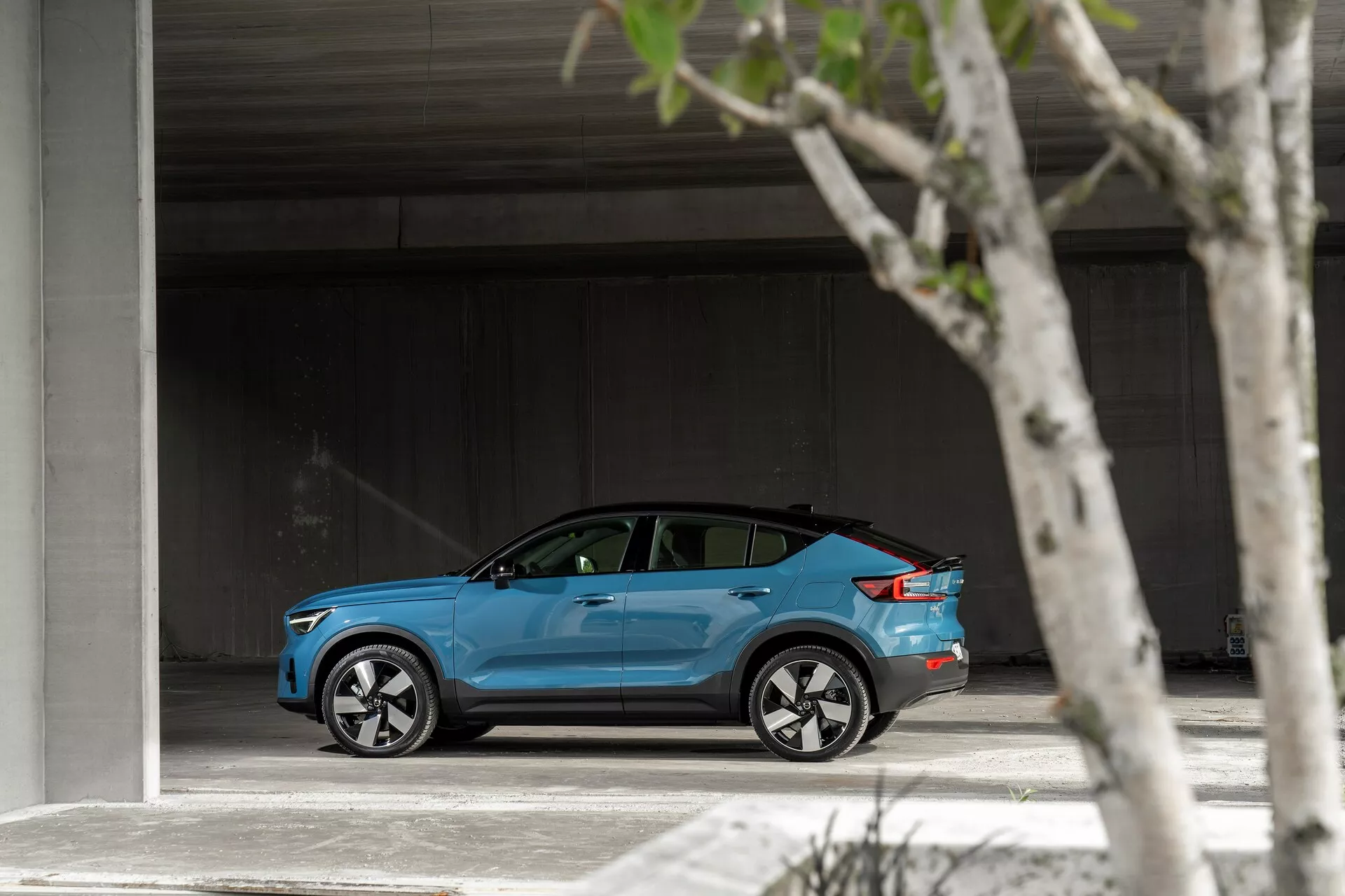 Profilo laterale di una Volvo C40 2021 blu brillante parcheggiata in un'area spaziosa, che mostra il suo design elegante e moderno, ruote in lega argentate a più razze, finestre leggermente tinte e possibile copertura del porto di ricarica.