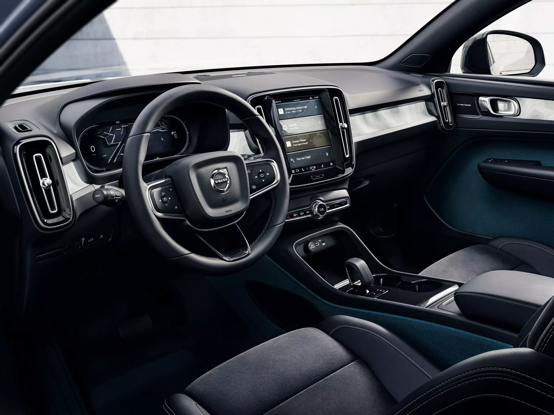 Immagine degli interni di una Volvo C40 del 2021 (1ª generazione) da una prospettiva esterna, che mostra l'abitacolo del conducente con volante, quadro strumenti digitale, console centrale con sistema di infotainment touch, comandi del clima, sedili ergonomici in tessuto scuro, pulsanti di controllo delle portiere e schema di colori a due toni con elementi di design moderni e funzionali.