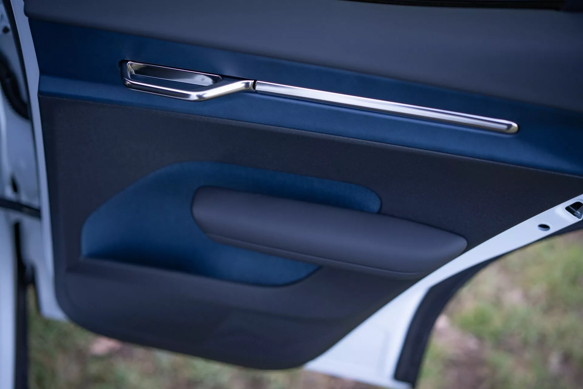 Primo piano dell'interno della porta della Volvo EX30 2024, con impugnatura metallica elegante, bracciolo ergonomico e tasca portaoggetti in una finitura scura di alta qualità