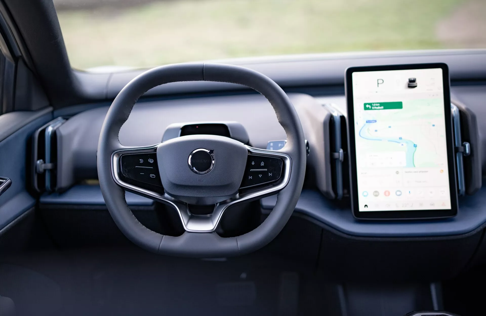 Vista interna della Volvo EX30 2024 che mostra il design moderno del volante e i quadranti digitali sul cruscotto, compreso il sistema di infotainment touchscreen verticale abilitato GPS.