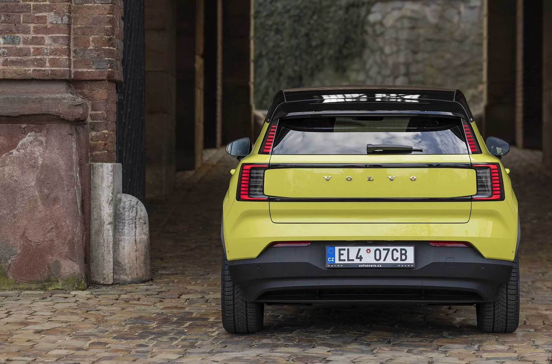 Vista posteriore del Volvo EX30 2024 su pavé che mostra eleganti luci posteriori orizzontali, emblema del produttore, targa europea, ampio lunotto con sbrinatore, spoiler sportivo e robusto paraurti con sensori di parcheggio