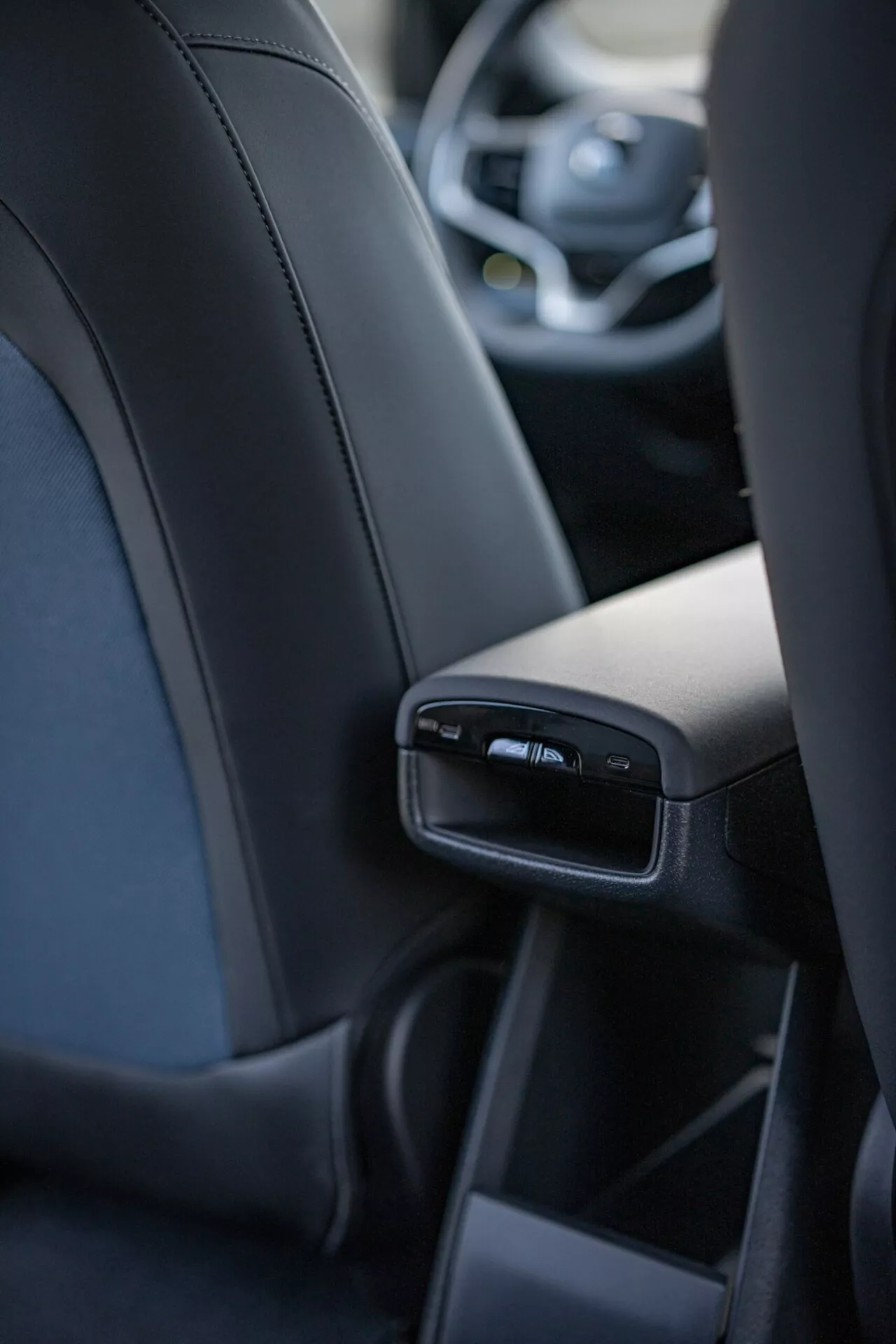 Vista interna del Volvo EX30 2024 focalizzata sulle caratteristiche dettagliate della consolle centrale posteriore dalla prospettiva del passeggero posteriore centrale, inclusi porte USB e bocchette d'aria, esibendo lusso e tecnologia