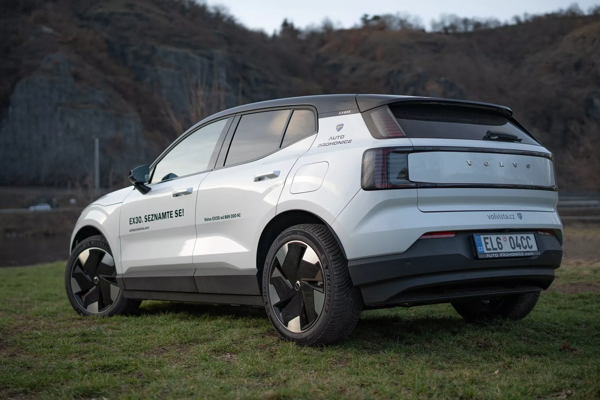 Vista posteriore a tre quarti del crossover elettrico Volvo EX30 2024 in bianco, che evidenzia il suo design moderno, cerchi in lega, sensori di parcheggio e funzioni di assistenza alla guida