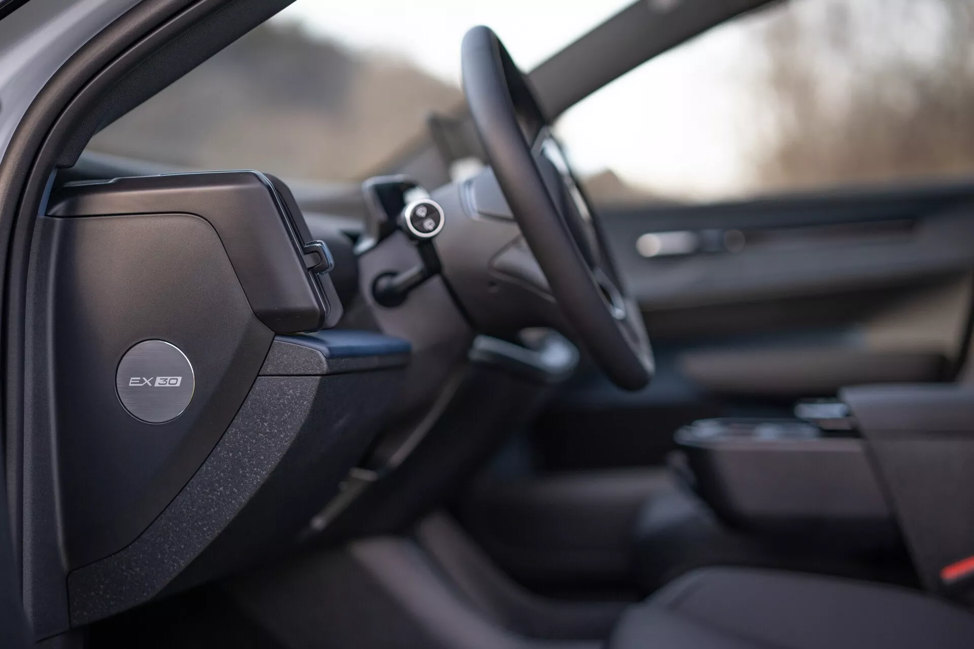 Vista interna del Volvo EX30 2024 focalizzata sul lato conducente con design del sedile sportivo o premium dettagliato, sistema audio Harman Kardon sul montante B, volante multifunzione e accenni di un avanzato sistema di infotainment e design del pannello della porta del passeggero
