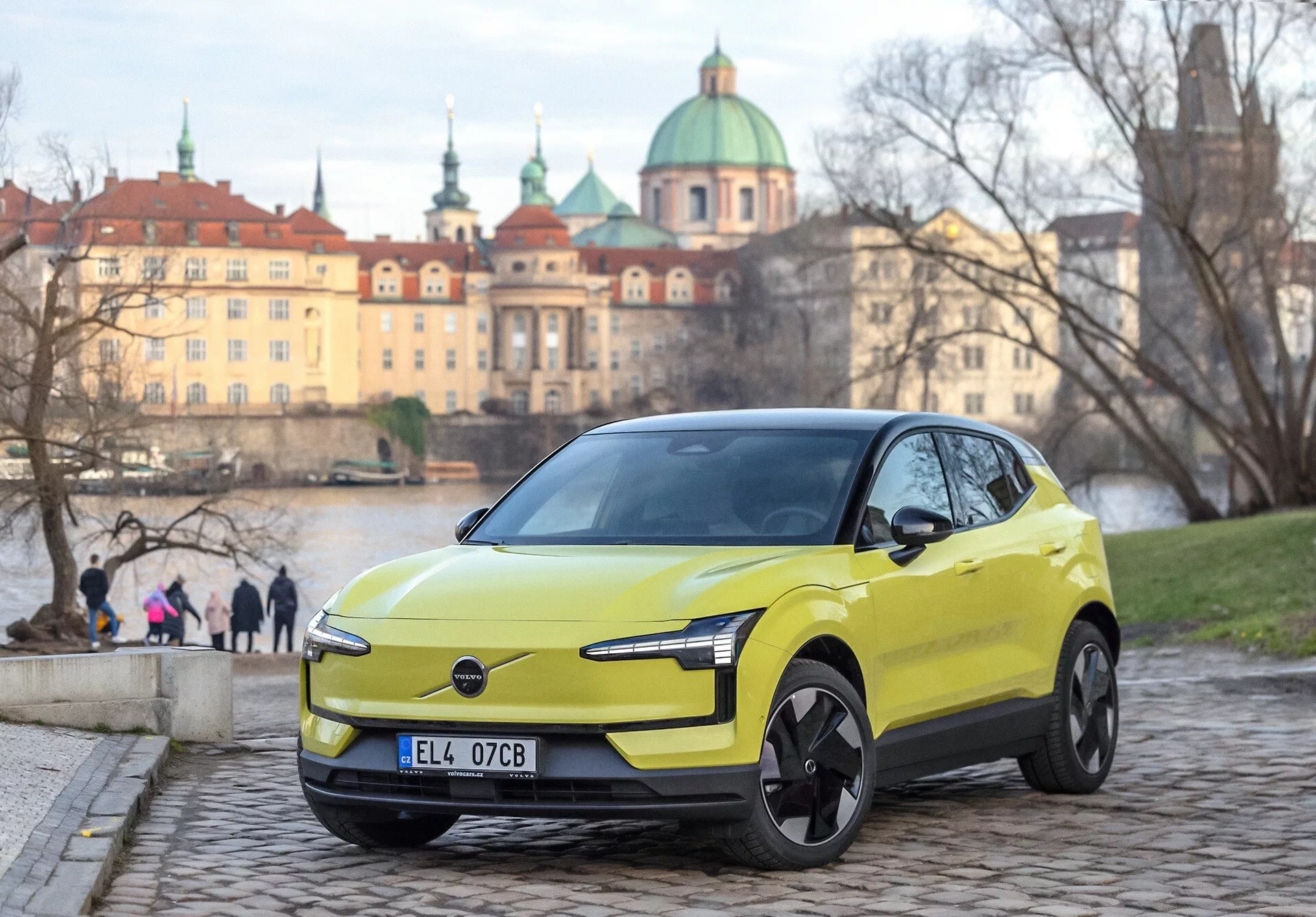 Volvo EX30 2024 in verde lime, vista frontale a tre quarti su sanpietrini, con fari LED moderni e caratteristiche di design elettrico, sfondo urbano europeo