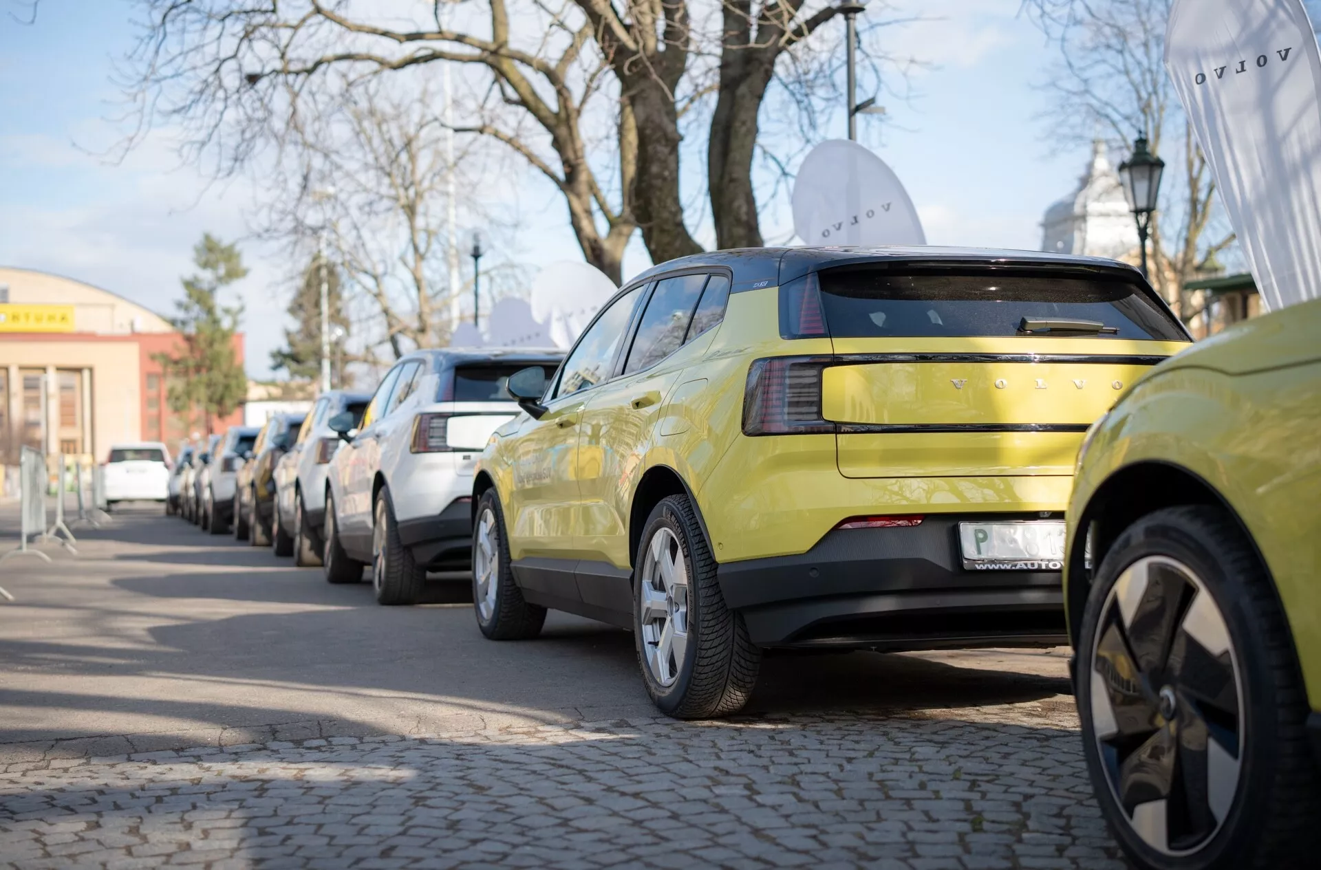 Volvo EX30 del 2024 in verde lime, mostra la vista posteriore con configurazione di luci posteriori LED e cerchi in lega a più razze, parcheggiata lungo una strada urbana