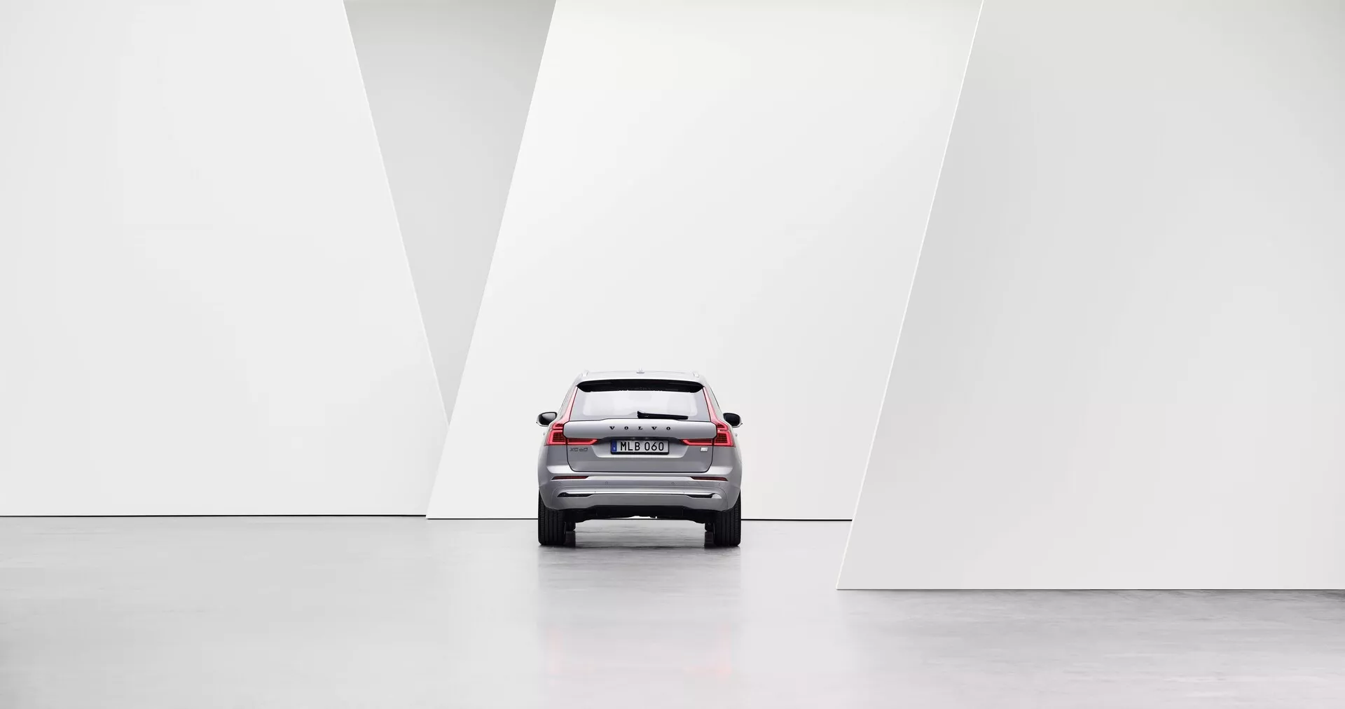 Prospettiva posteriore centrata di un'auto che mostra elementi di design moderno, tra cui fanali posteriori a LED, parabrezza posteriore, coperchio del bagagliaio e paraurti posteriore in un ambiente minimalista, luminoso e simmetrico con pavimenti lucidi e pareti bianche geometriche.