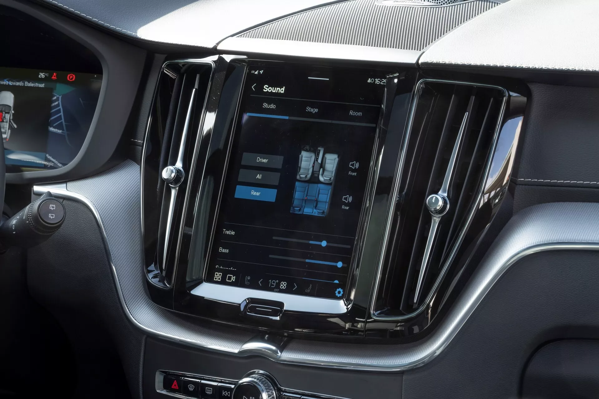 Immagine dell'interno di una Volvo XC60 2021 facelift, concentrata sulla console centrale con un grande sistema di infotainment touchscreen orientato verticalmente. Scattata dalla prospettiva del sedile del passeggero, l'immagine mostra anche le impostazioni del climatizzatore bi-zona, le feritoie di ventilazione in metallo e i pulsanti di controllo manuali sotto lo schermo, emanando un design moderno e lussuoso.