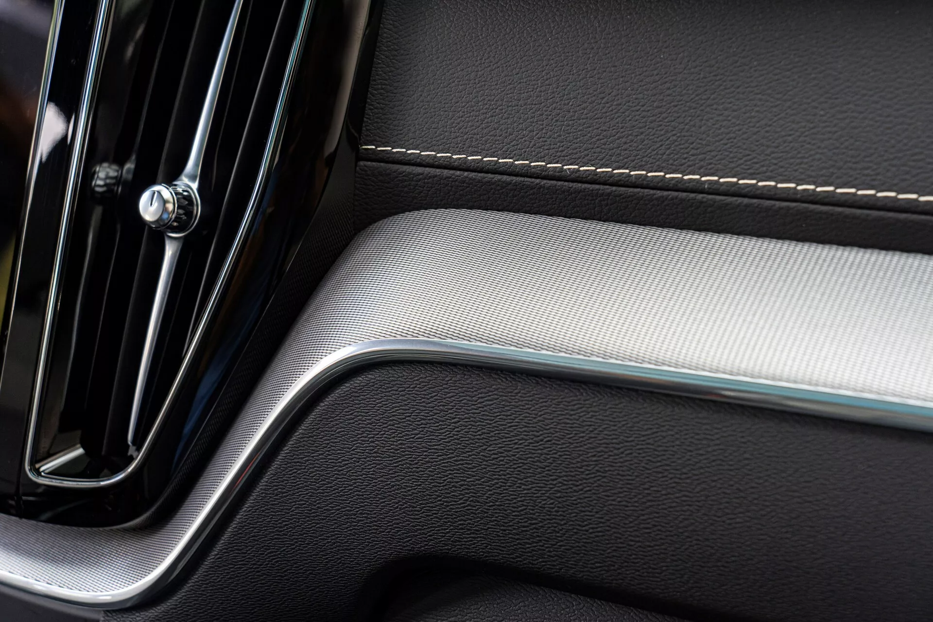 Primo piano di una sezione del pannello della porta interna di un'auto, che mostra un design moderno ed elegante. Il pannello presenta una maniglia della porta come il cromo con eleganza minimalista, cuciture precise su rivestimenti in pelle e un inserto in metallo spazzolato che aggiunge contrasto di texture, riflettendo lusso e artigianato di qualità.