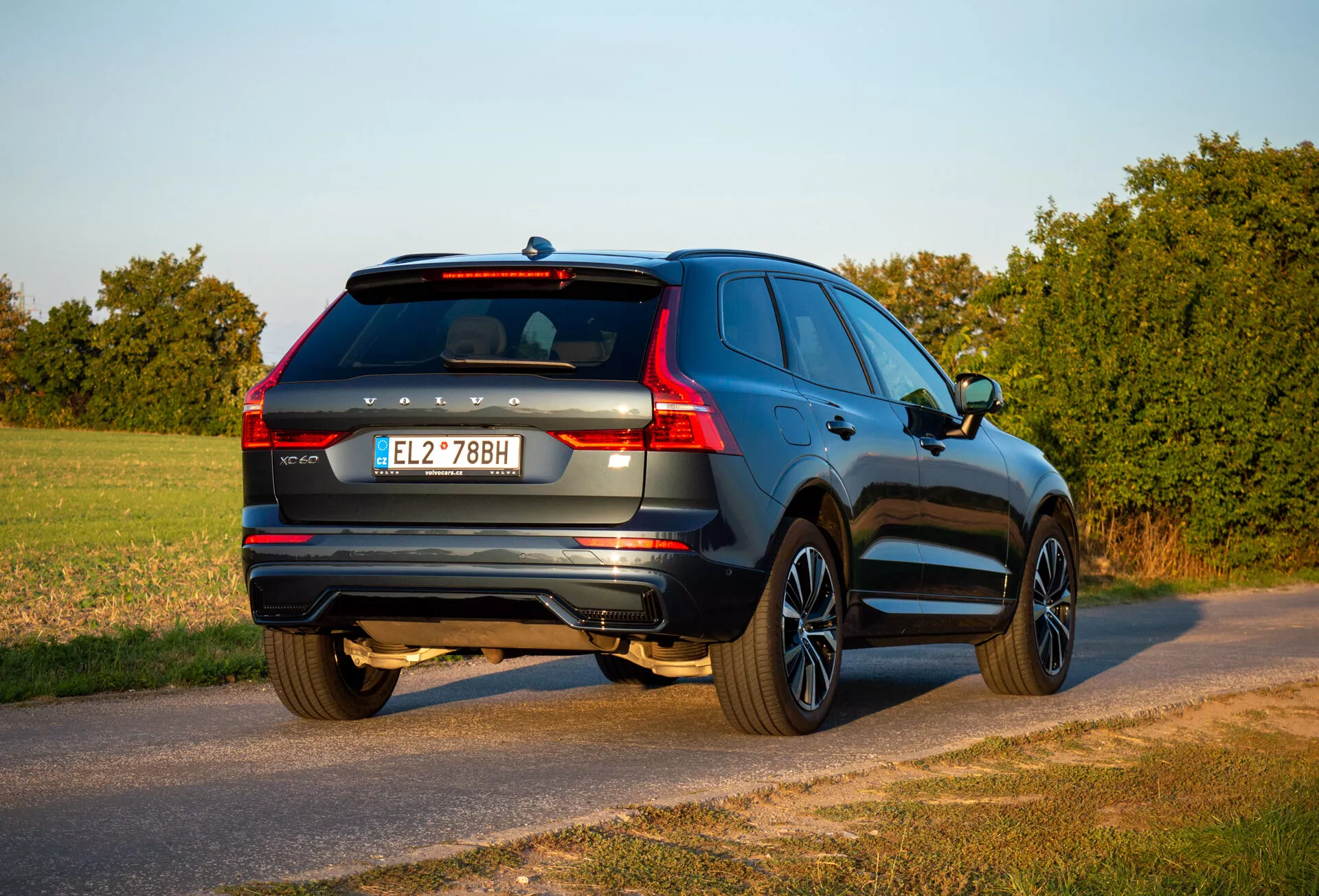 SUV Volvo XC60 Recharge ibrido plug-in 2021 in vista da tre quarti posteriore parcheggiato su una strada di campagna durante l'ora d'oro con estremità posteriore, lato passeggero, dettagli del portellone posteriore e caratteristiche di design visibili