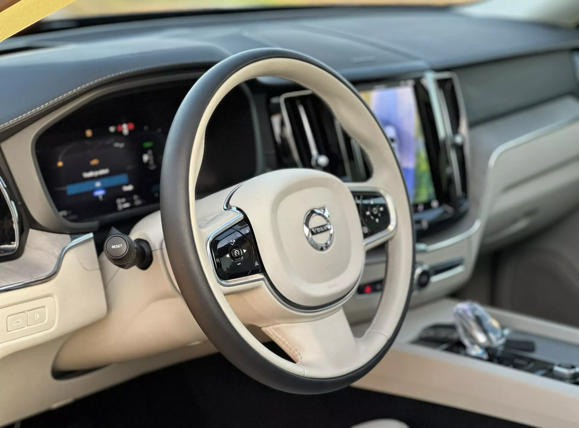 Vista interna del Volvo XC60 Recharge Plug-In Hybrid 2021 che mostra il volante e il cruscotto digitale dalla prospettiva del conducente, evidenziando i controlli per il cruise control, la gestione audio, il sistema infotainment touchscreen e finiture di lusso