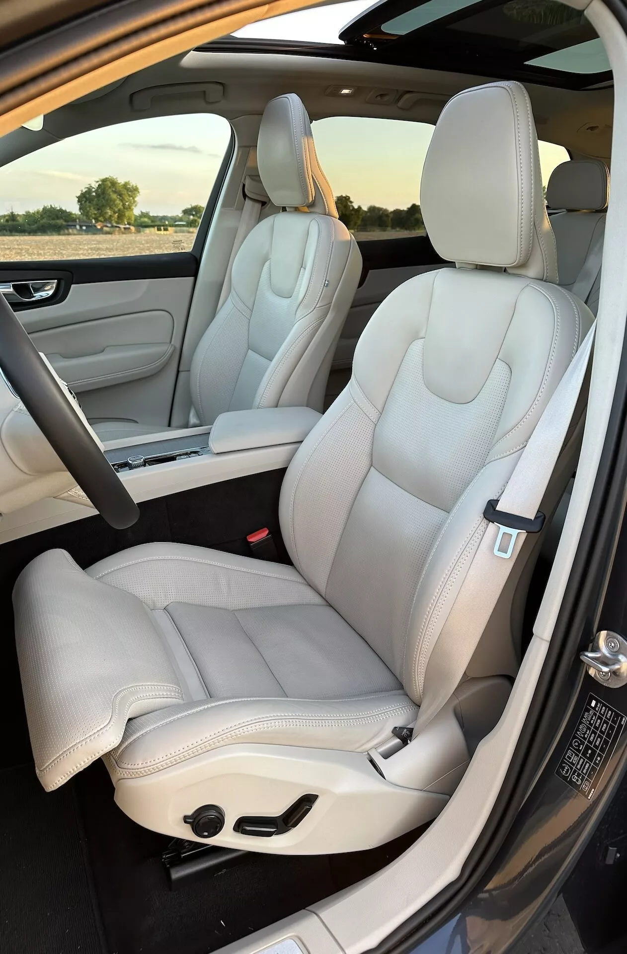 Vista interna Volvo XC60 Recharge ibrido plug-in 2021: sedili anteriori e parziali posteriori, tappezzeria in pelle chiara di lusso, design moderno, sedili regolabili elettricamente con eleganti cuciture, scattata dall'esterno della porta lato passeggero di giorno