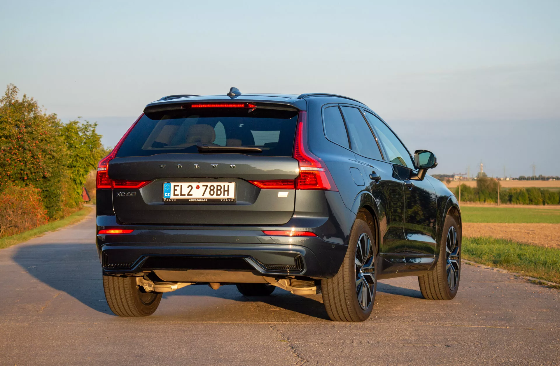 SUV Volvo XC60 Recharge ibrido plug-in 2021 fermo su una strada lastricata che mostra la sua vista posteriore a tre quarti, evidenziando i fanali posteriori LED, le ruote in lega e il design dinamico in un contesto rurale sotto cieli sereni