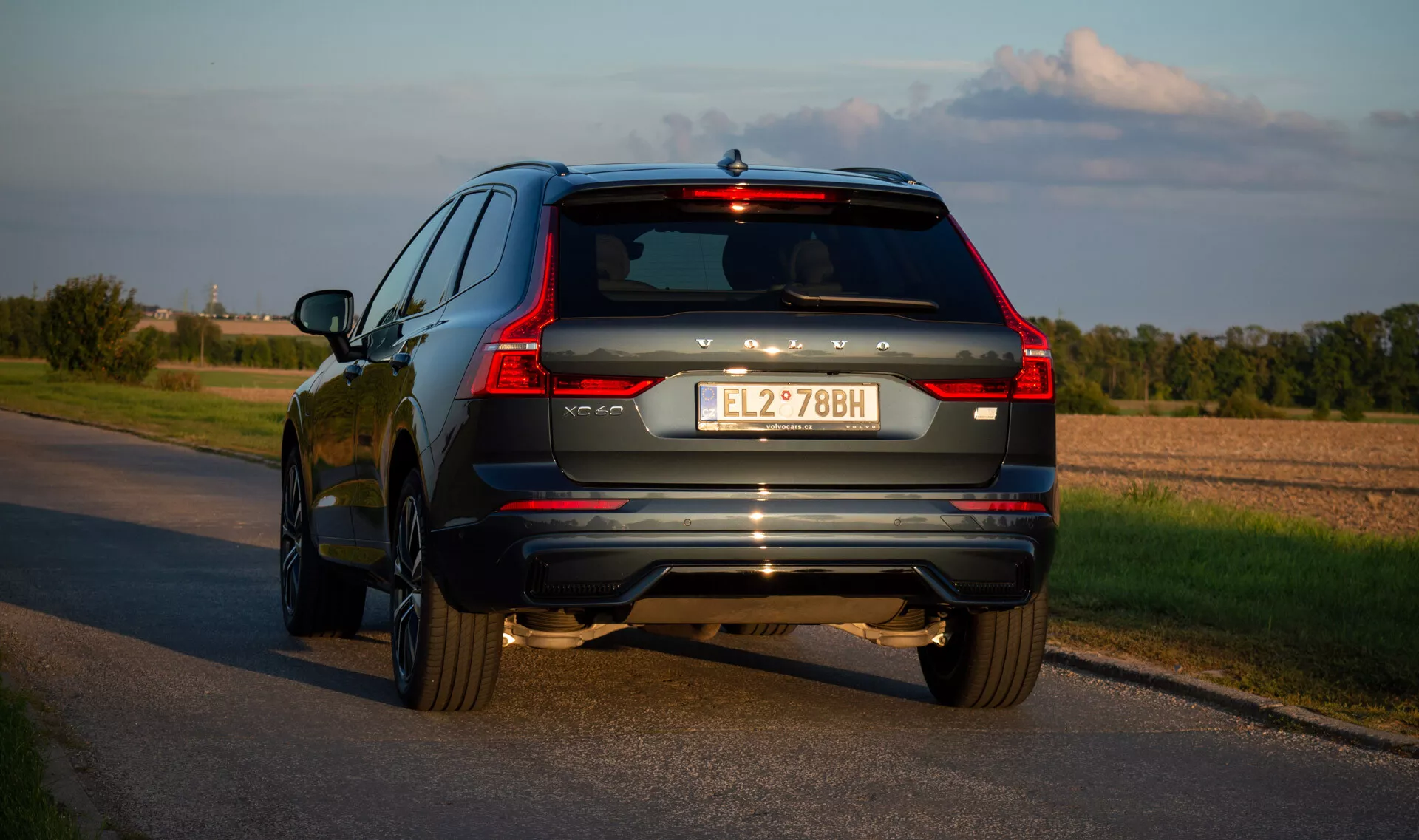 SUV Volvo XC60 Recharge ibrido plug-in 2021 su strada d'asfalto, ripresa da un angolo posteriore di tre quarti che evidenzia i fari posteriori a LED del veicolo, sistema di scarico e accenti cromati durante il tardo pomeriggio