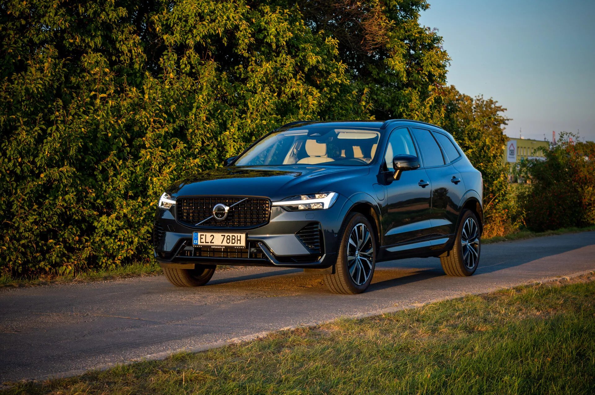 Volvo XC60 Recharge Plug-In Hybrid 2021 parcheggiata a bordo strada nel tardo pomeriggio con illuminazione calda, mostrando griglia anteriore, fari LED e profilo sportivo su sfondo di vegetazione