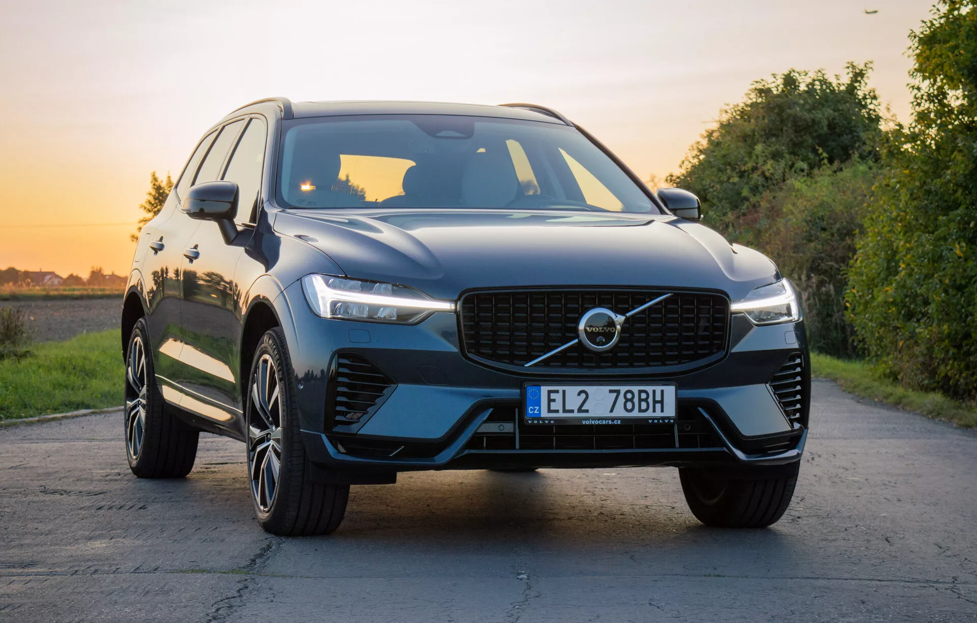 SUV di lusso Volvo XC60 Recharge Plug-In Hybrid 2021 su strada asfaltata con paesaggio naturale durante l'ora d'oro, mostrando griglia anteriore, fari LED, cofano scolpito, ruote in lega a più razze e finitura lucida