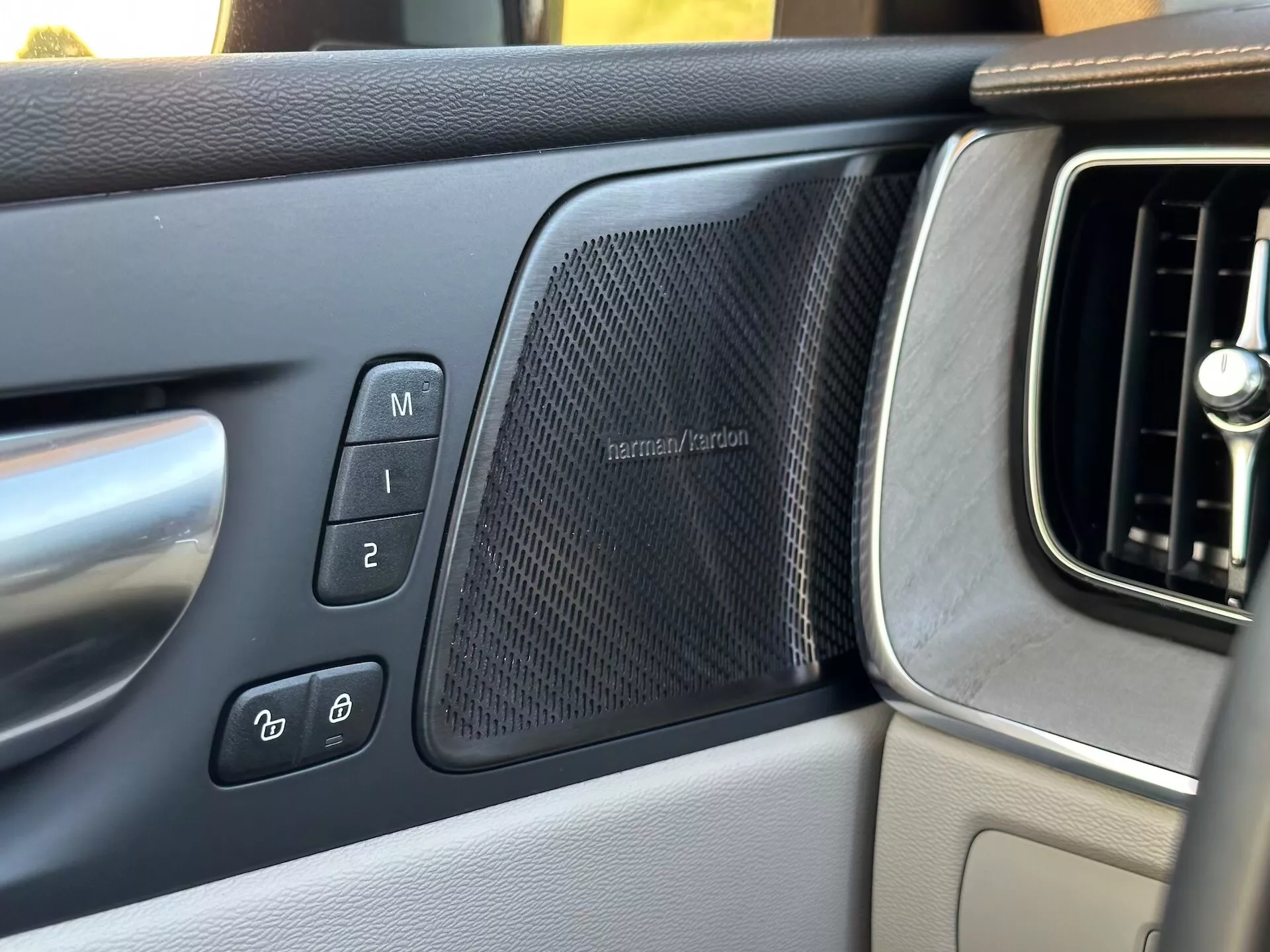 Vista interna Volvo XC60 Recharge Plug-In Hybrid 2021 sul pannello della porta lato guidatore con impostazioni memoria sedile, controlli serratura elettronica porte, griglia altoparlante harman/kardon e parte della bocchetta di aerazione del cruscotto