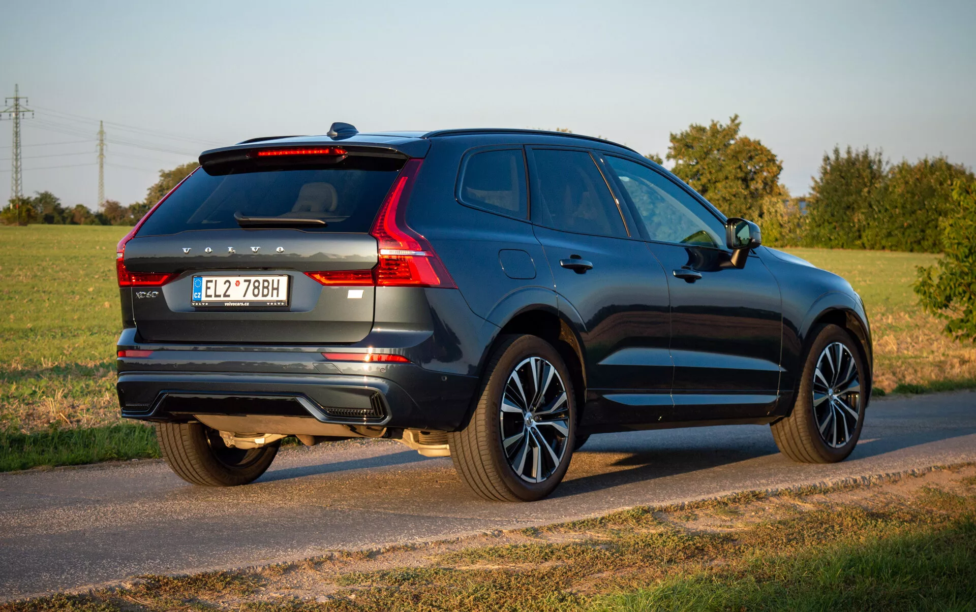 Volvo XC60 Recharge Plug-In Hybrid del 2021 in blu profondo, mostra il suo design aerodinamico e funzionalità moderne come luci posteriori LED, cerchi in lega e sistema di scarico doppio, parcheggiata su una strada di campagna sotto il cielo chiaro