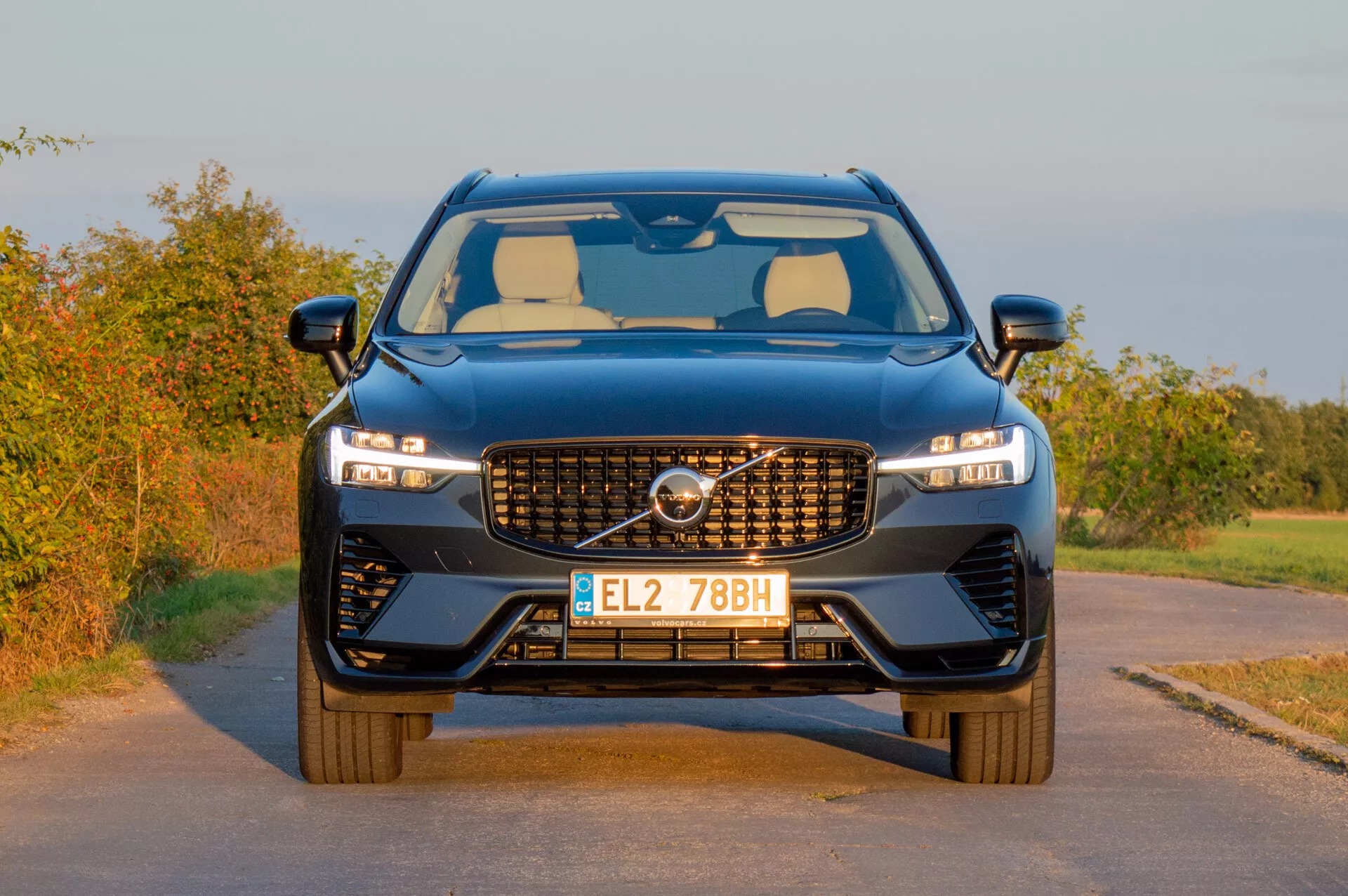 Volvo XC60 Recharge Plug-In Hybrid 2021 che mette in mostra il suo design moderno con una griglia distintiva, fari LED snelli e un fascione anteriore sportivo su uno sfondo rurale in luce calda del tardo pomeriggio