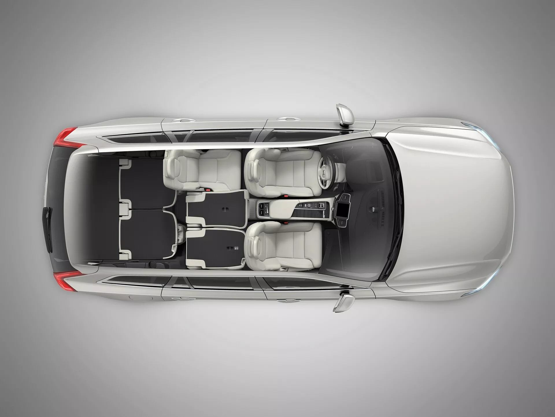 Vista dall'alto di una berlina Volvo XC90 di seconda generazione del 2015 con tetto trasparente o rimosso digitalmente che mostra l'interno. L'immagine rivela il lungo cofano anteriore dell'auto, quattro porte chiuse, quattro ruote e la configurazione dei sedili con due sedili anteriori e un sedile posteriore a panca per tre passeggeri. Consolle centrale e leva del cambio visibili. Mostrato il cruscotto a guida a sinistra con volante, display e disposizione dei comandi. Elementi di design come poggiatesta, specchietti esterni e spazio e disposizione interni sono chiaramente visibili.