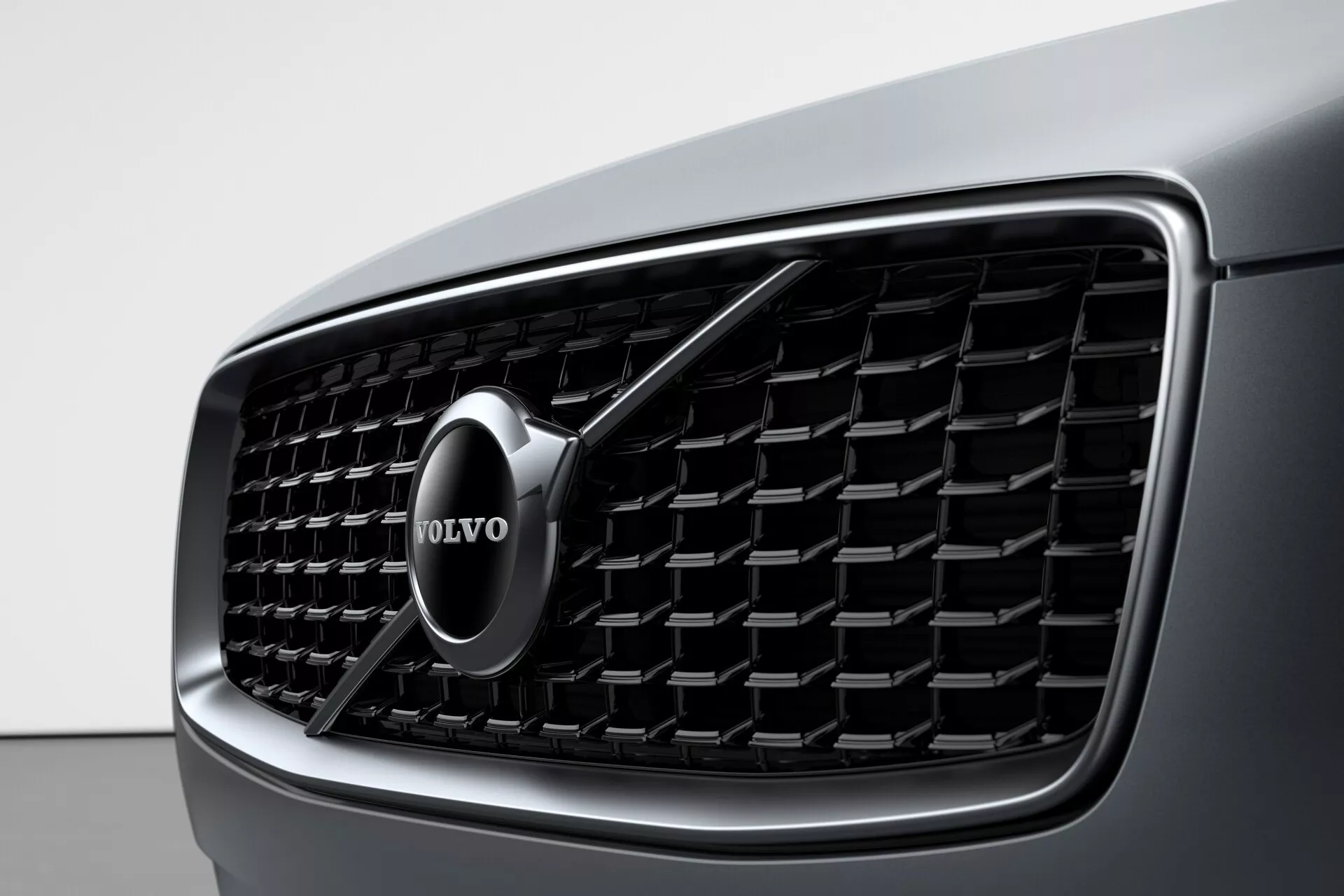 Vista ravvicinata della griglia anteriore di una Volvo XC90 2015 (seconda generazione), che mostra il design dettagliato e il prominente emblema del marchio Volvo. La griglia presenta lamelle verticali e un bordo cromato, enfatizzando il lusso e l'estetica moderna.