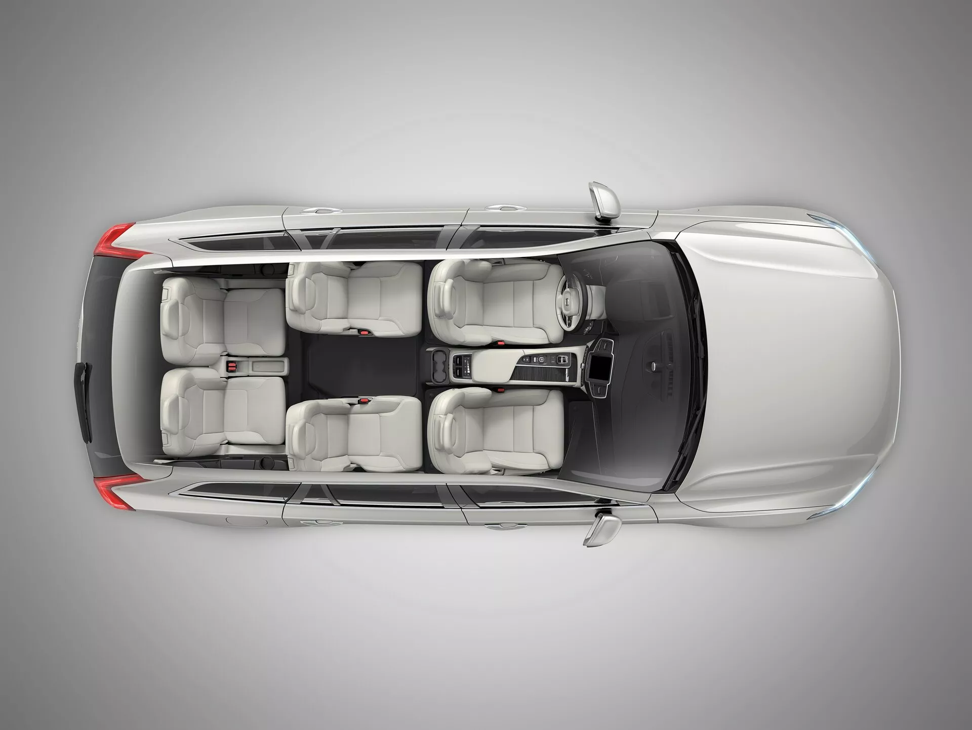 Veduta dall'alto di una Volvo XC90 2015 (2a generazione) che mostra il suo esterno grigio metallizzato argento, carrozzeria SUV a quattro porte, finestre con protezione UV oscurata, interni con configurazione per sette posti con sedili grigi chiari e cerchi in lega. L'immagine mette in evidenza caratteristiche inferite come ADAS, sicurezza del veicolo, sistema di infotainment, climatizzazione multizona, ingresso senza chiave e sistemi di assistenza al parcheggio, con illuminazione da studio che garantisce una chiara messa a fuoco sul design dettagliato dell'auto.