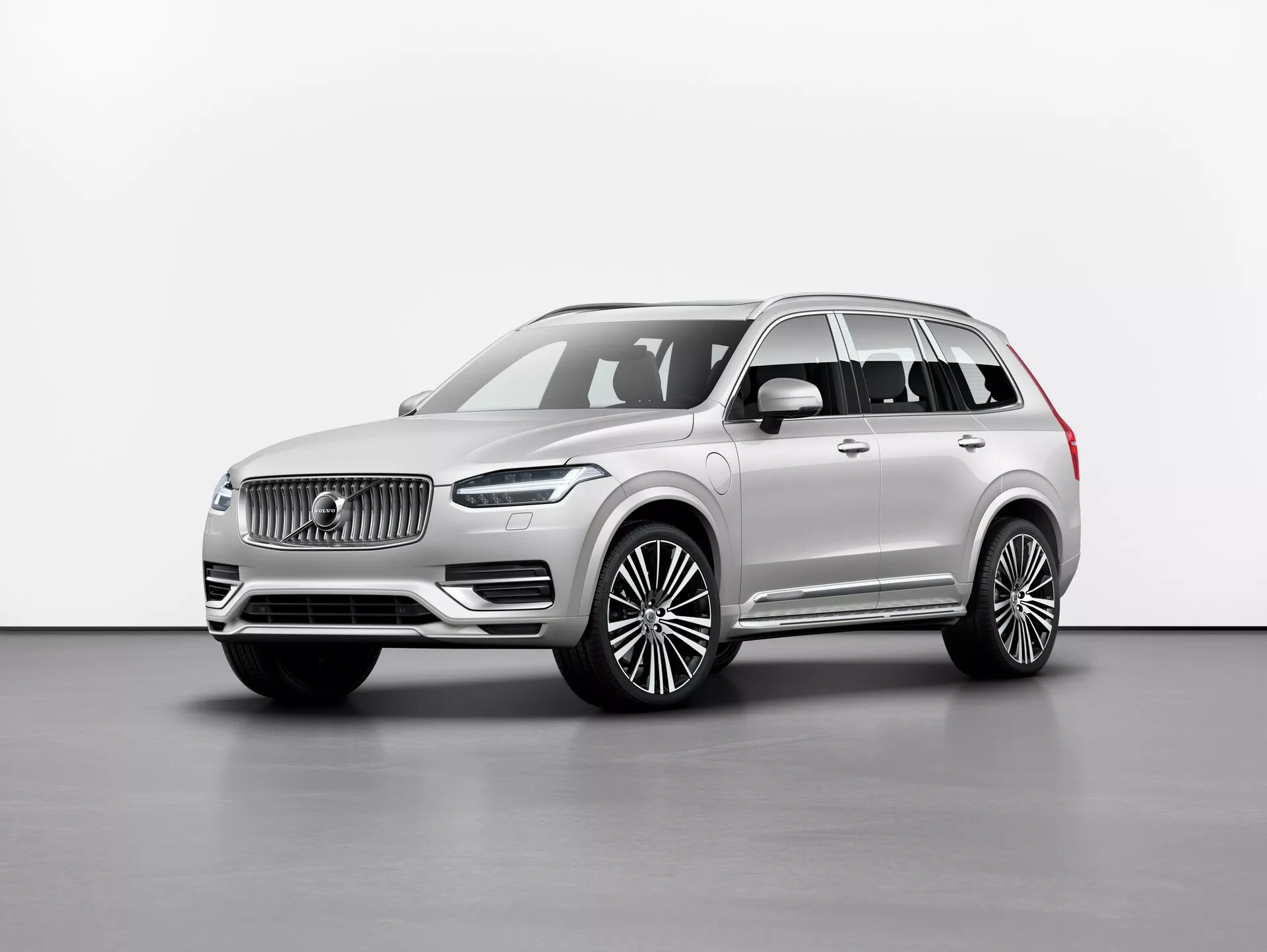 Fotografia in studio di un SUV di lusso Volvo XC90 2015 (2ª generazione), raffigurato da un angolo frontale di tre quarti che mostra la griglia anteriore con un logo distintivo, eleganti fari a LED, un ampio paraurti anteriore e un lungo passo con grandi cerchi in lega. Gli specchietti laterali si trovano sotto il montante A con finestre rifinite con modanature cromate e barre sul tetto. Il colore neutro della vernice emana raffinatezza e l'immagine mette in risalto le linee e i contorni dell'auto con una illuminazione uniforme su uno sfondo semplice. Le caratteristiche probabili includono tecnologie di assistenza alla guida e sistemi di infotainment avanzati.