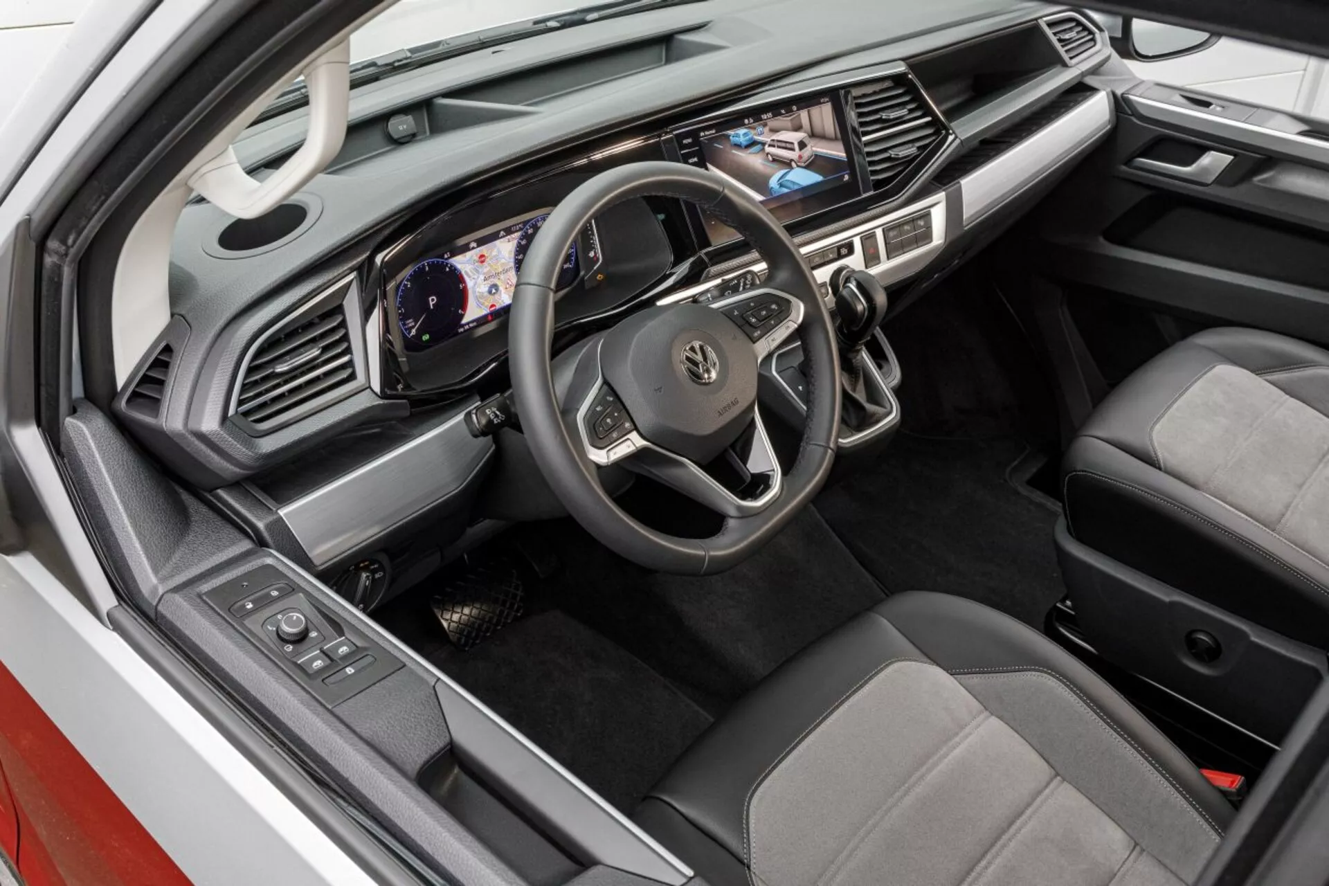 Vista dall'alto dell'interno del Volkswagen Nutzfahrzeuge Transporter 2019 (T6.1 California) che mostra l'area del conducente con cruscotto digitale, schermo multimediale touch e sedili rivestiti in due tonalità